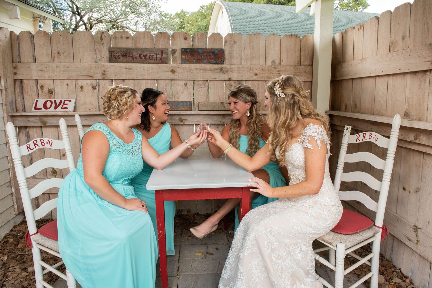Wedding party sits together on rustic white rocking chairs on a wooden porch wearing turquoise dresses and formal attire. Rum River Barn Mil