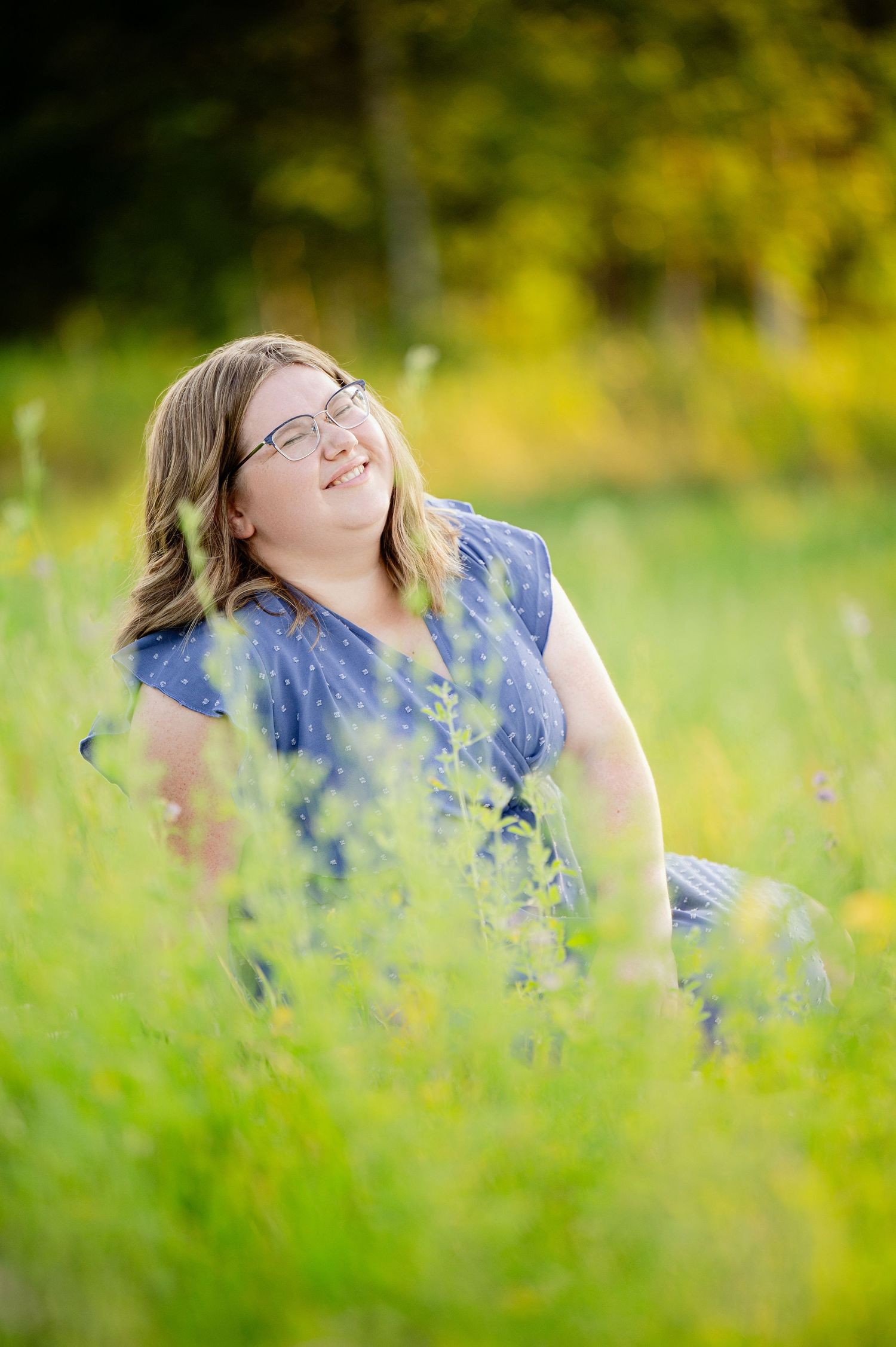 Senior Portrait in Foreston MN Person laying in a field of wildflowers wearing blue on a sunny summer day.