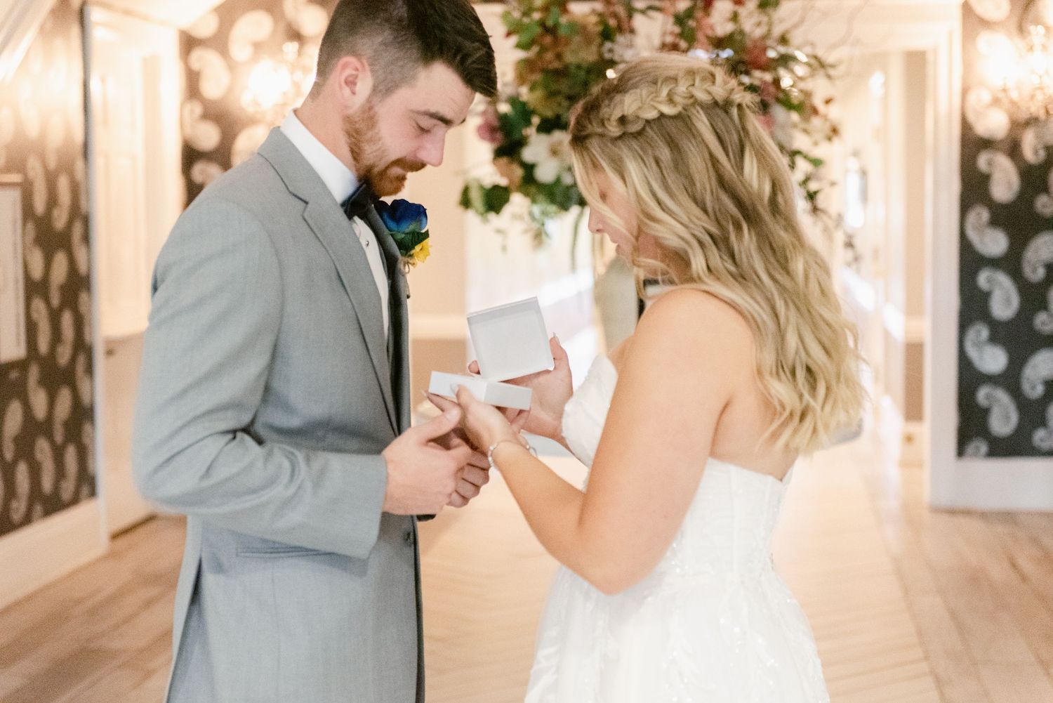 Two people share a sweet emotional first look moment at an elegant indoor wedding venue with glowing lights.