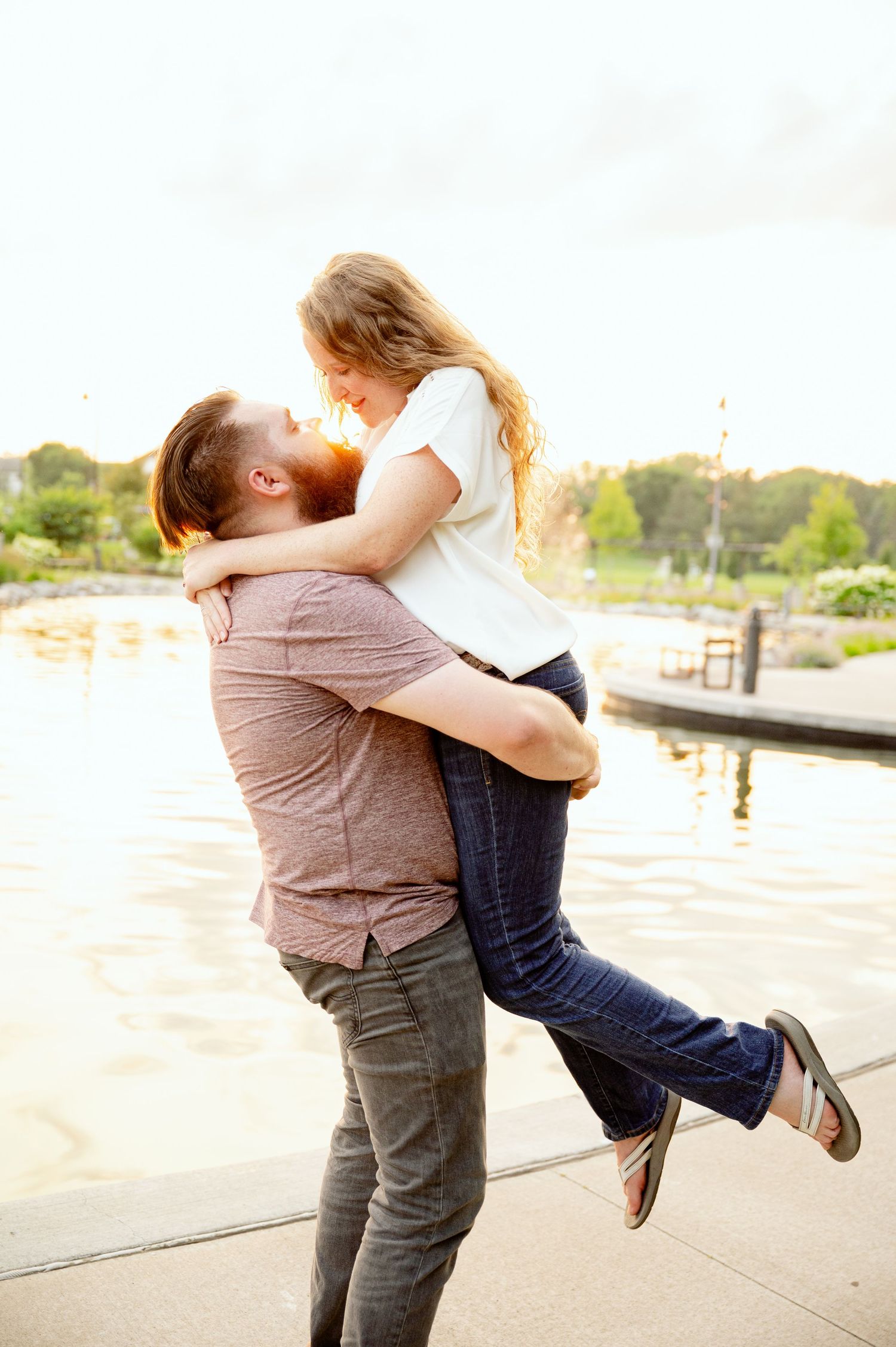 A romantic couple embraces by the waterfront during golden hour sunset.