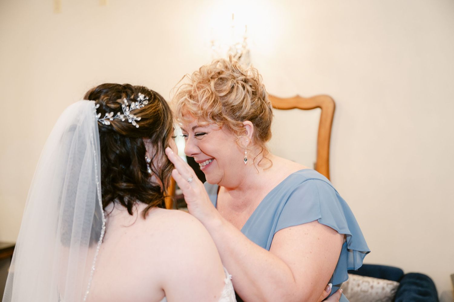 An emotional shared moment during wedding preparations shows tender interaction against a light background.