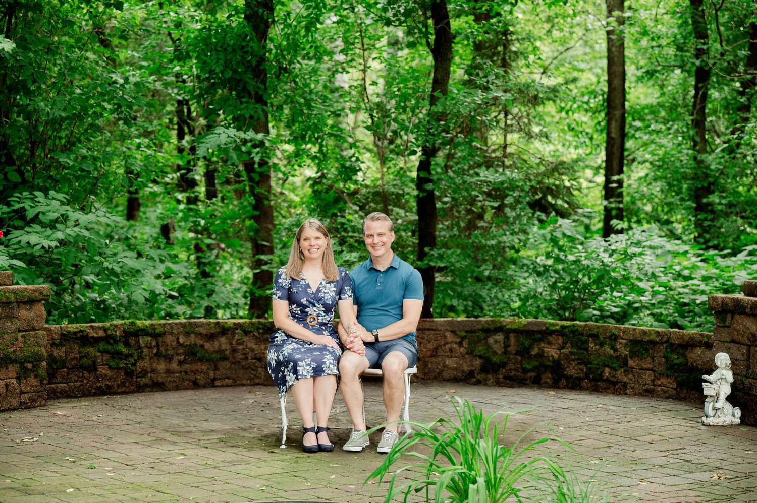 Clear Lake Family Photography: Two people sit together on a curved stone bench surrounded by green forest and landscaping.