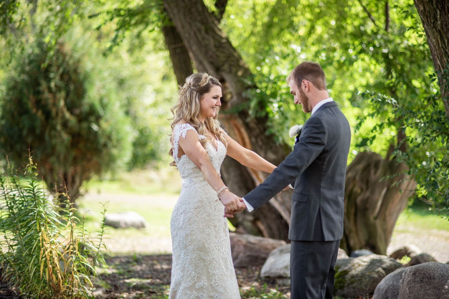A couple shares an intimate moment outdoors under green trees during their wedding celebration.