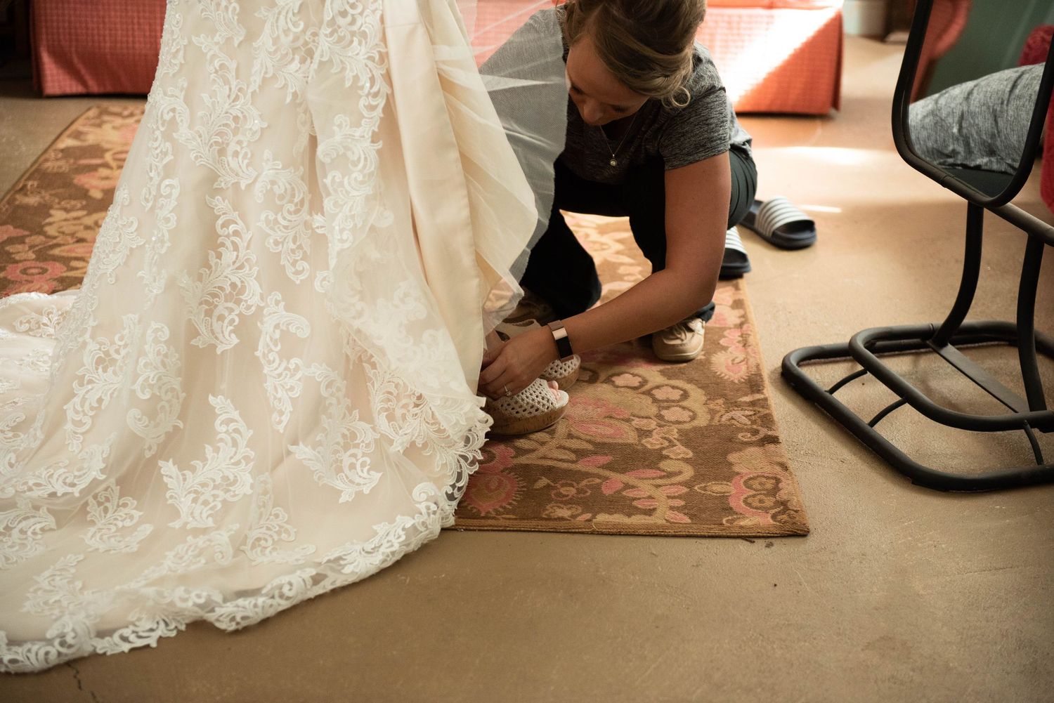 Various detail shots showing the hemline and intricate lace details of a white wedding dress against a carpet. Rum River Barn Milaca Minneso