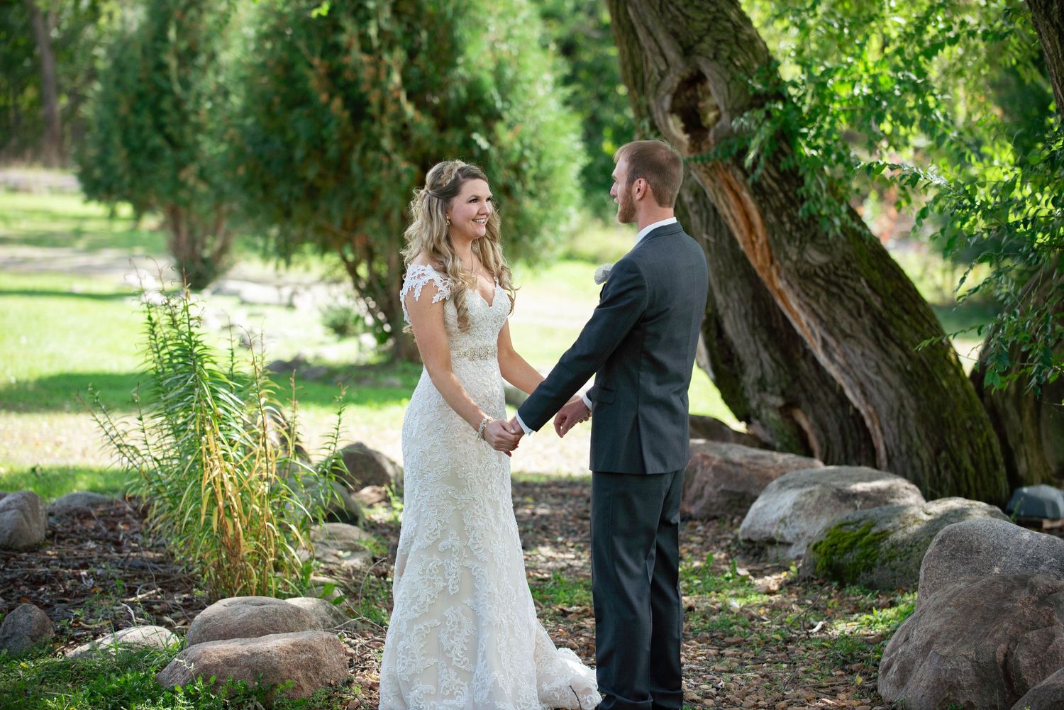 A couple shares a romantic moment in formal attire under large trees in a garden setting. Rum River Barn Milaca Minnesota Weddings
