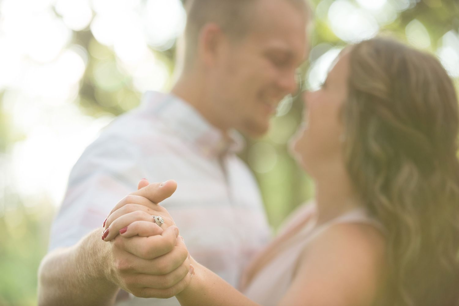 Couple dancing and laughing together outdoors in a romantic garden setting with soft sunlit background.