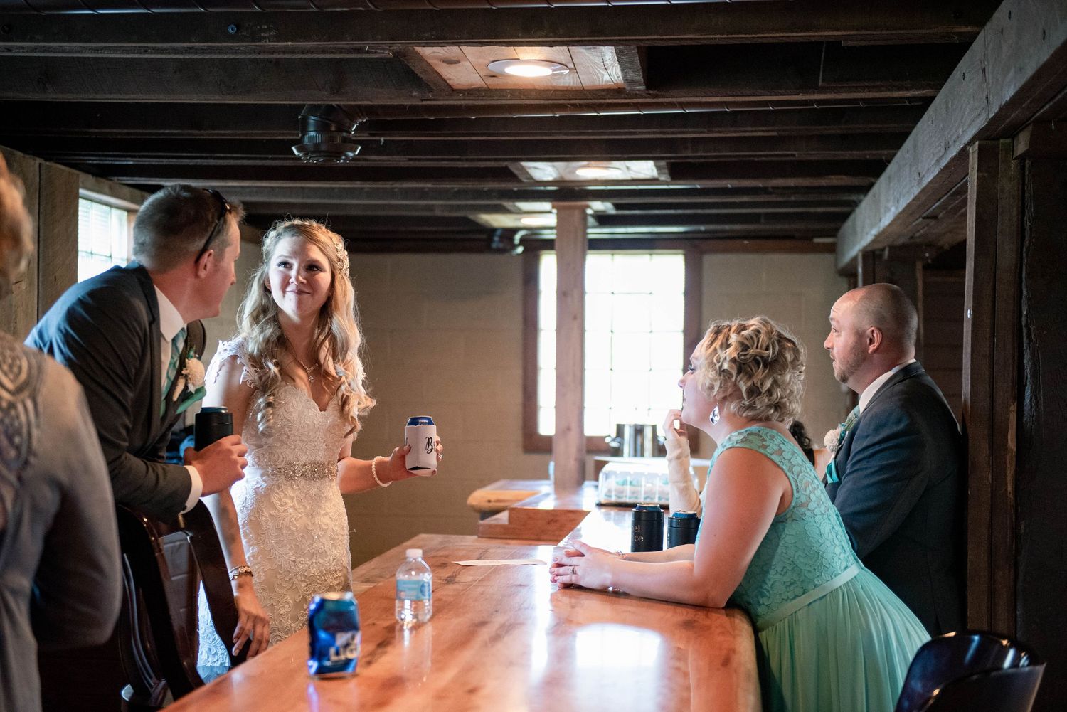 Wedding reception gathering at a rustic wooden bar with indoor lighting and exposed wooden beams. Rum River Barn Milaca Minnesota Weddings