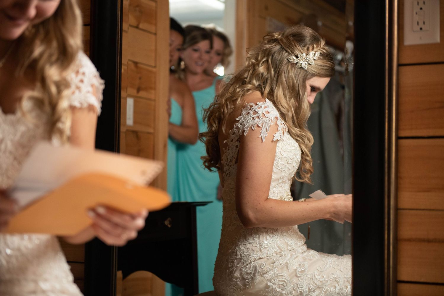 A bride in lace gown reads a letter while standing in a wooden room. Rum River Barn Milaca Minnesota Weddings