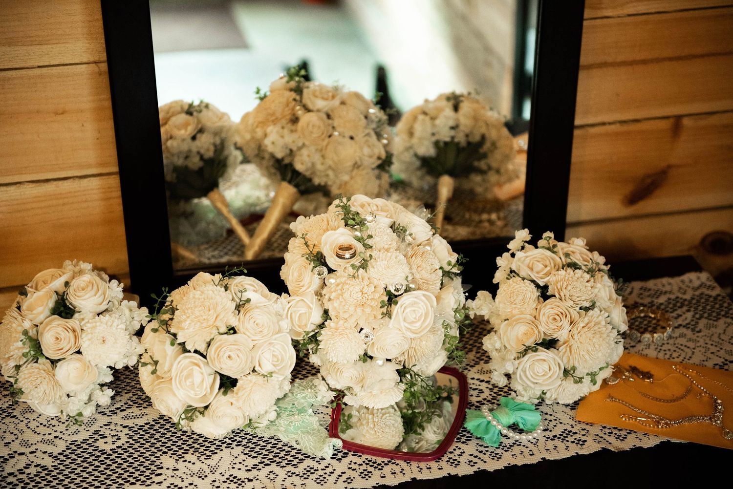 White floral wedding bouquets arranged on lace tablecloth at rustic wooden venue.