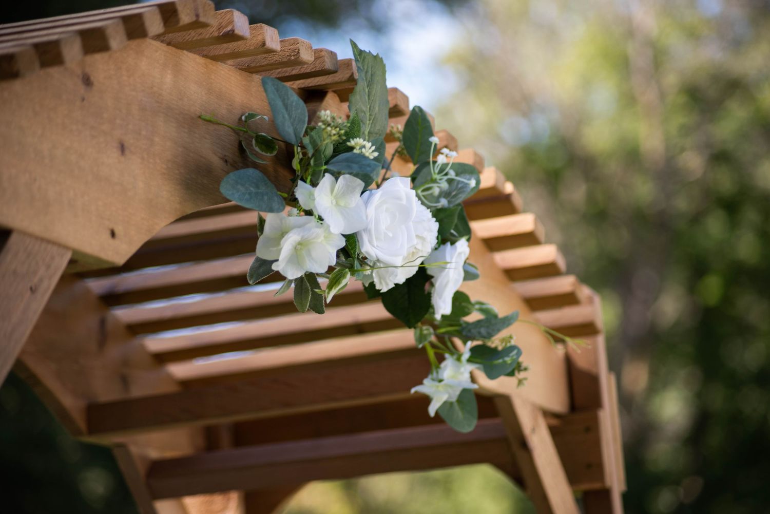 White floral decorations adorn wooden pergola structure in outdoor garden setting.