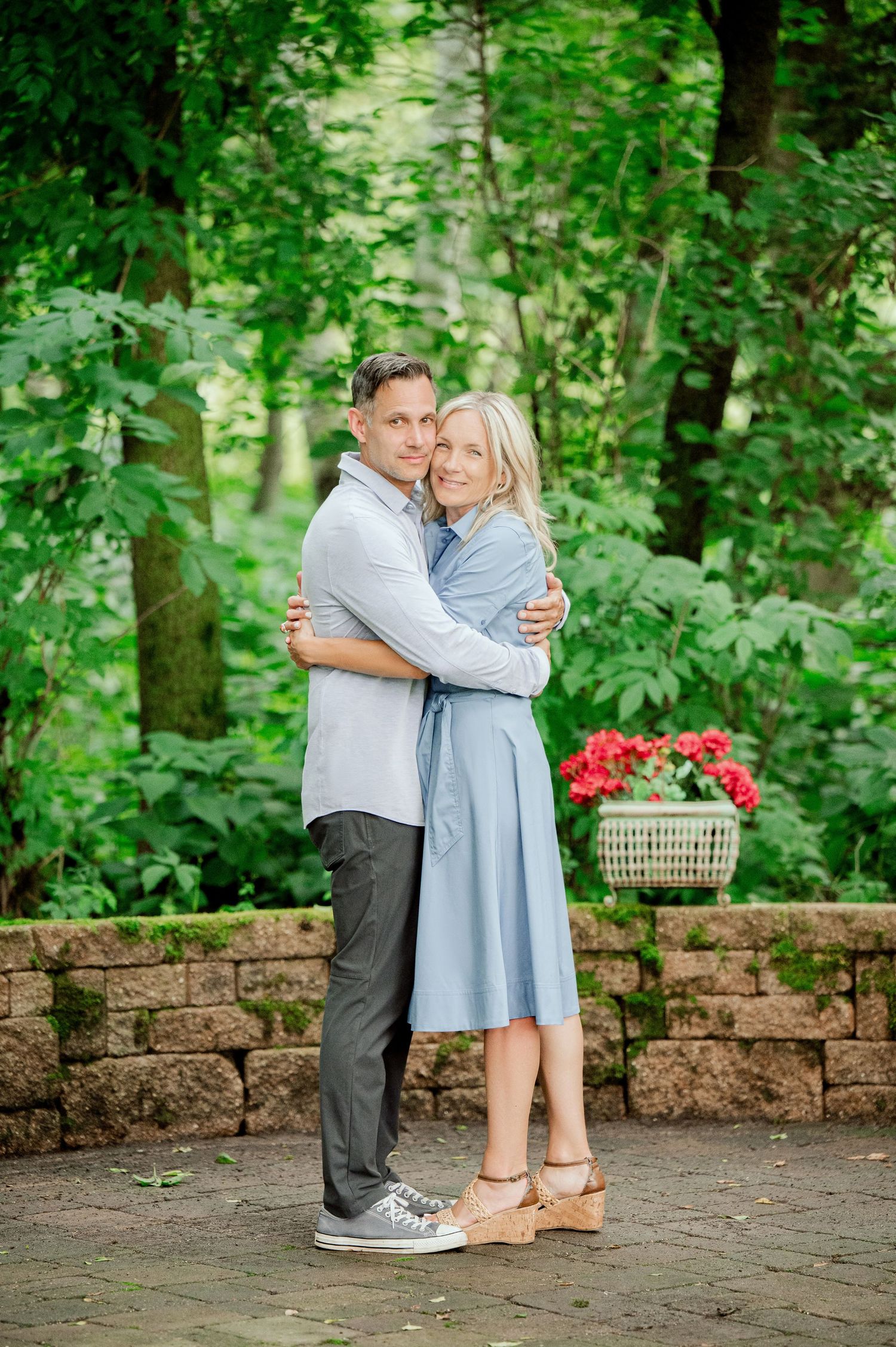 Clear Lake MN Family Photos: A romantic couple embraces on a brick patio with a wicker basket of red flowers in the background.