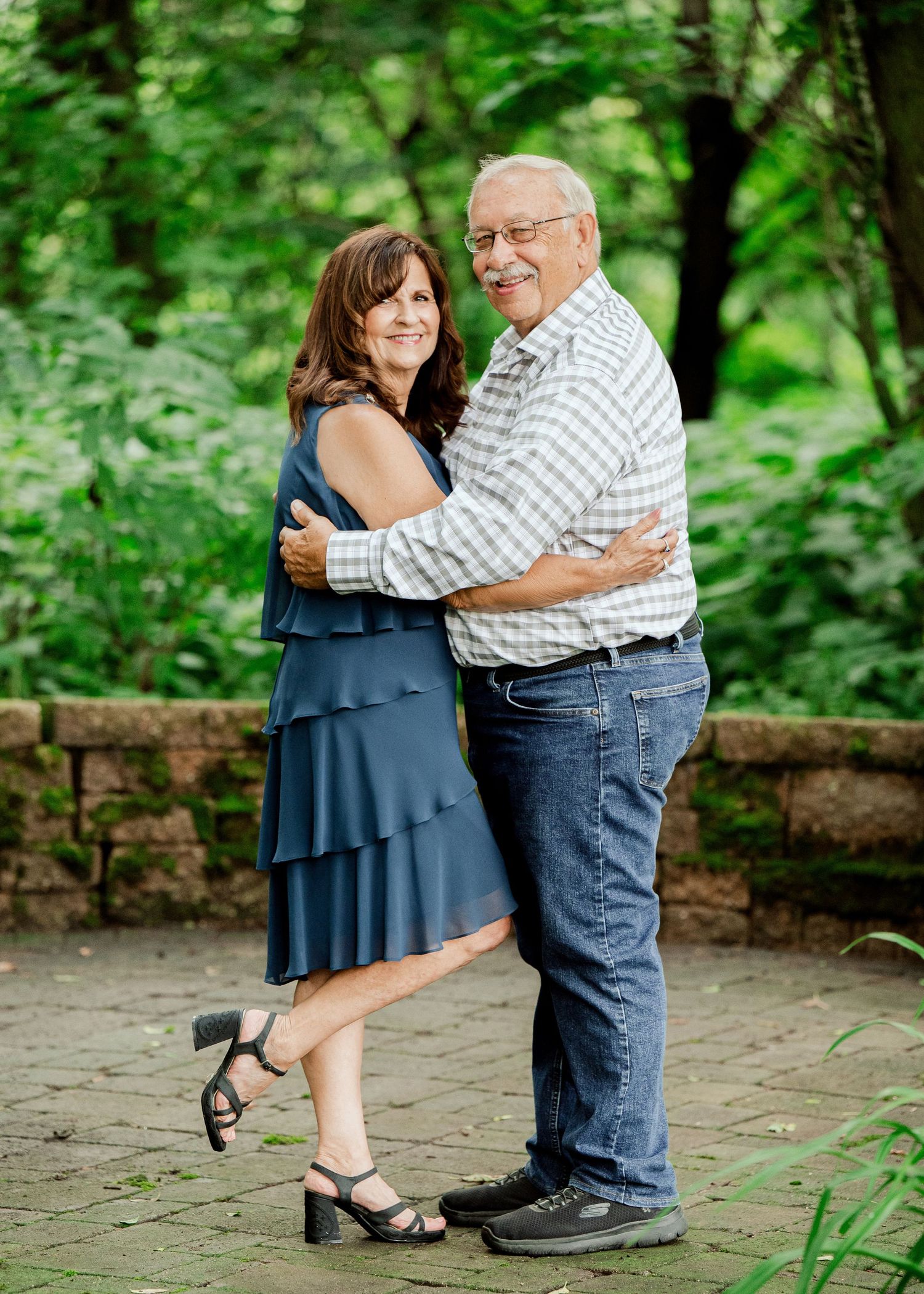 Clear Lake MN Family Photos: A couple shares a romantic dance pose on a stone patio with lush green forest surroundings.