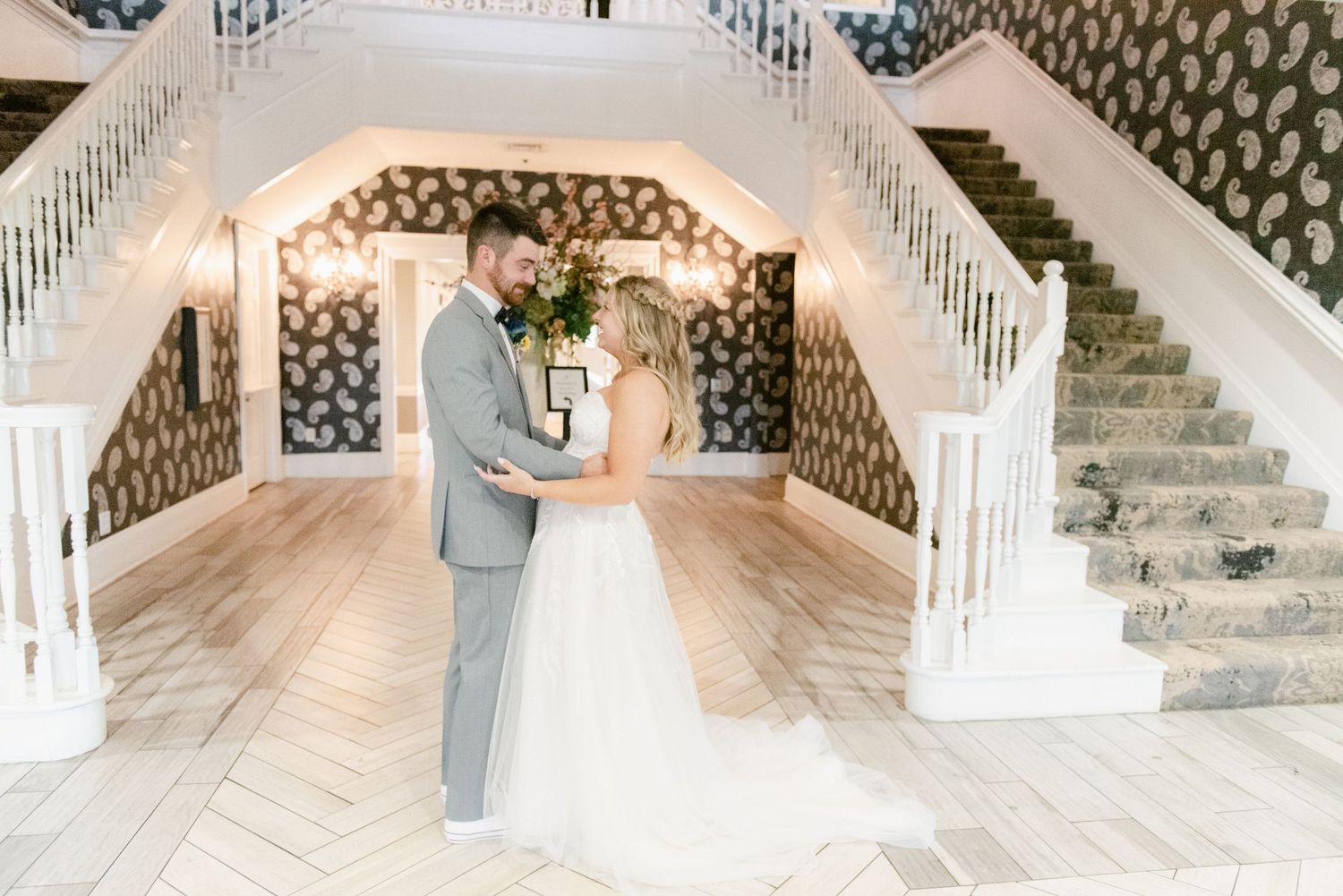 Panoramic view of a grand staircase with white railings and decorative wallpaper in a wedding venue.