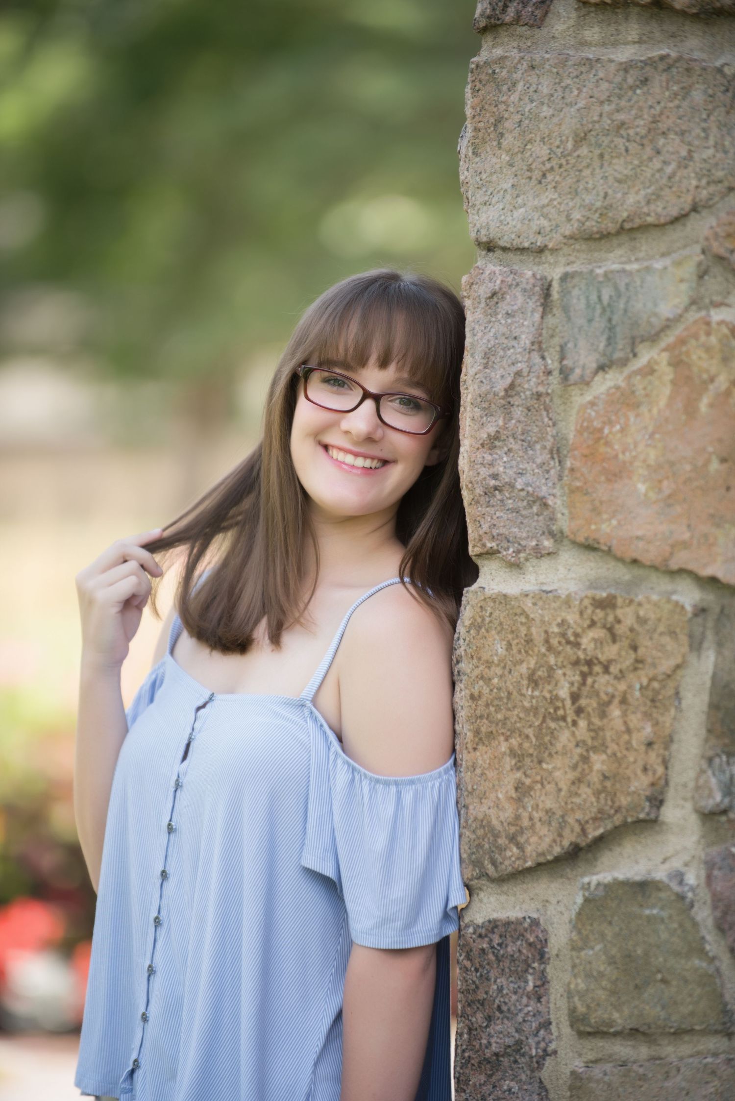 Senior Portrait at St Cloud State College Person in light blue top posing against stone wall outdoors with natural lighting.