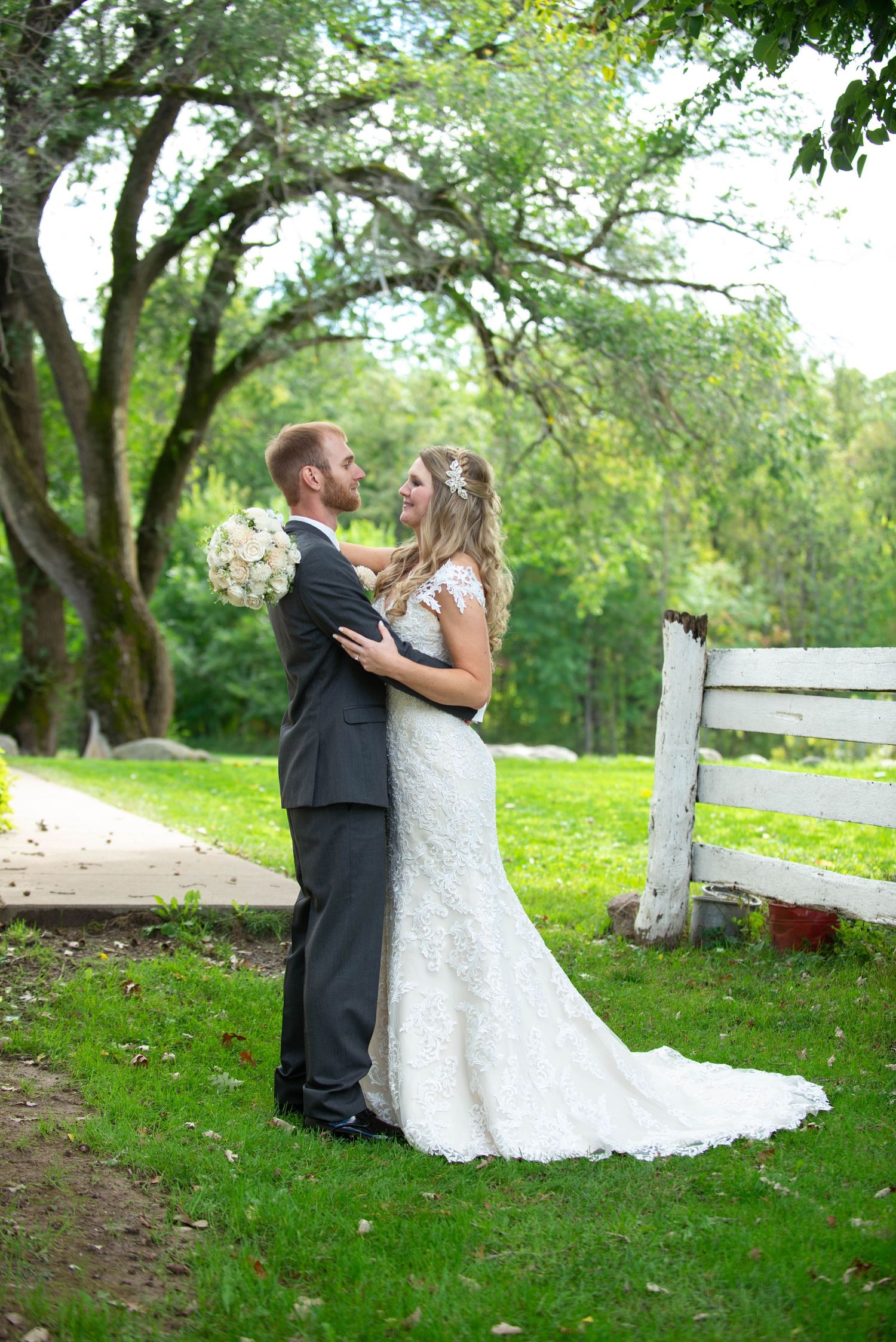 Couple shares intimate moment in lush garden setting with white fence and flowing wedding dress. Rum River Barn Milaca Minnesota Weddings