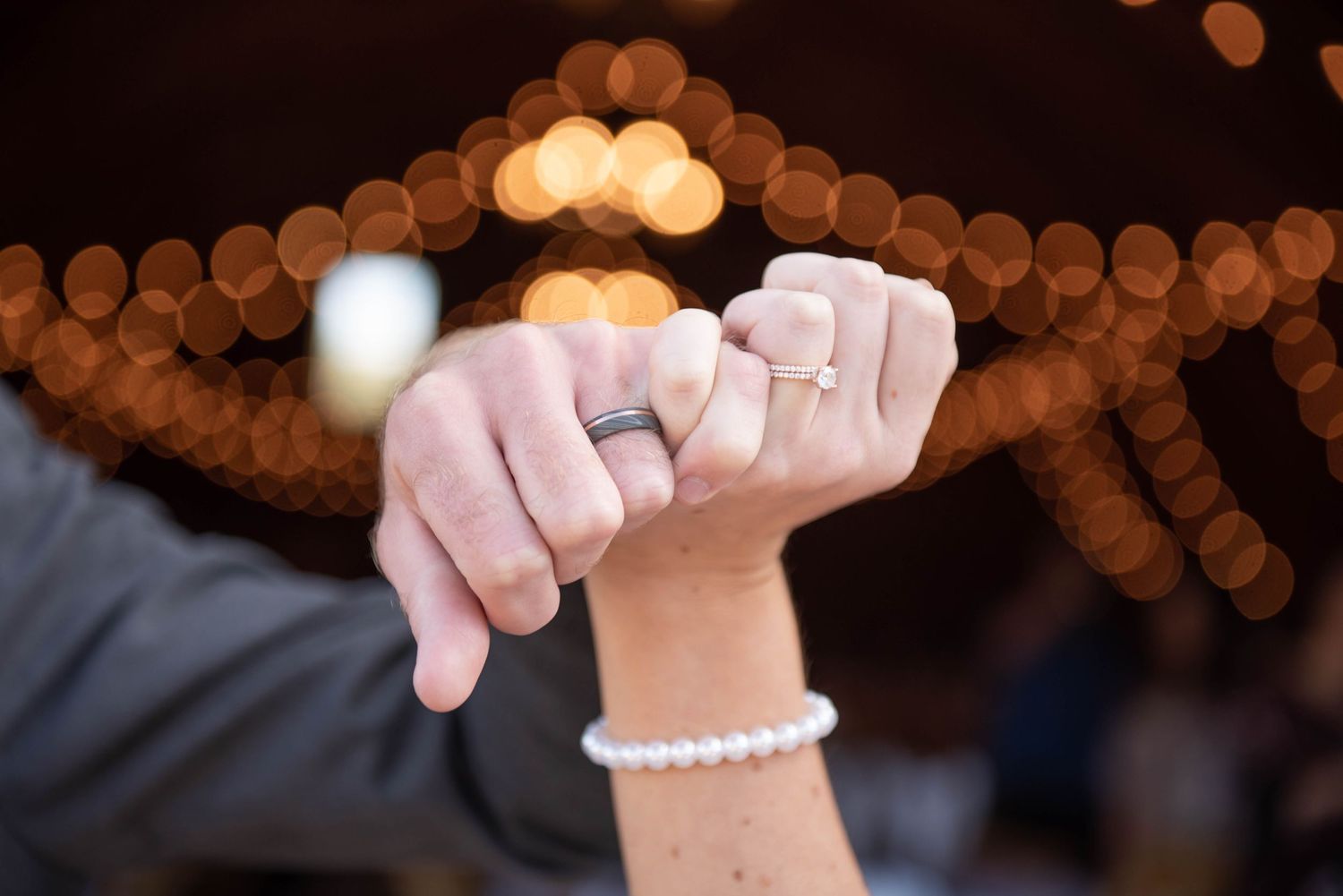 Hands with wedding rings shown against blurred bokeh lights background creating romantic ambiance. Rum River Barn Milaca Minnesota Weddings