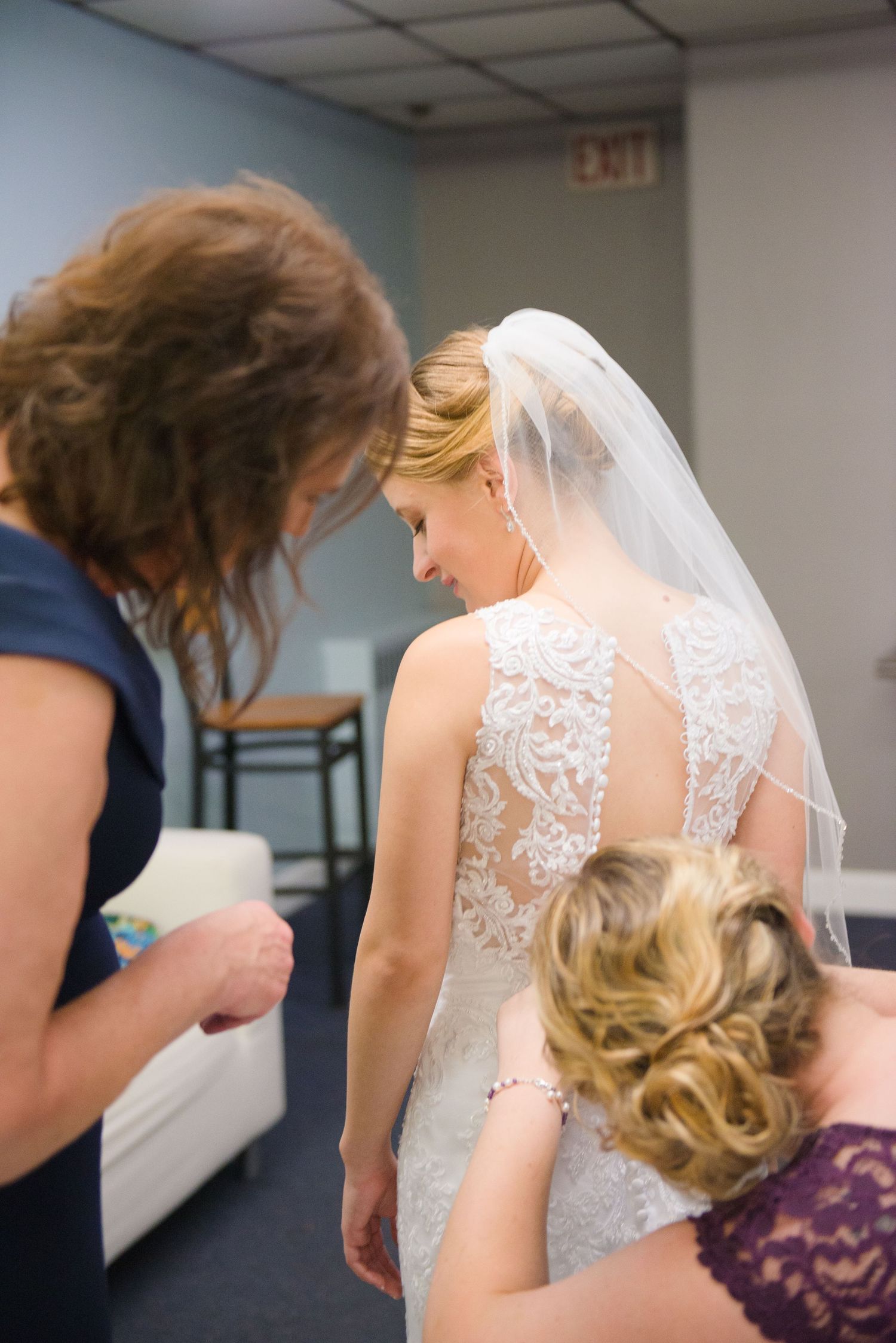 Wedding dress fitting scene showing intricate lace back details and attendants helping with final adjustments. Andover wedding at Magestic O