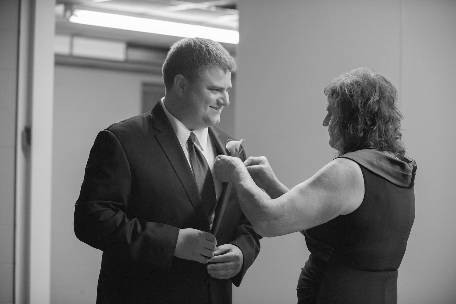 Someone helps adjust a boutonniere on a man's suit lapel in a black and white photo. Andover wedding at Magestic Oaks Golf Club