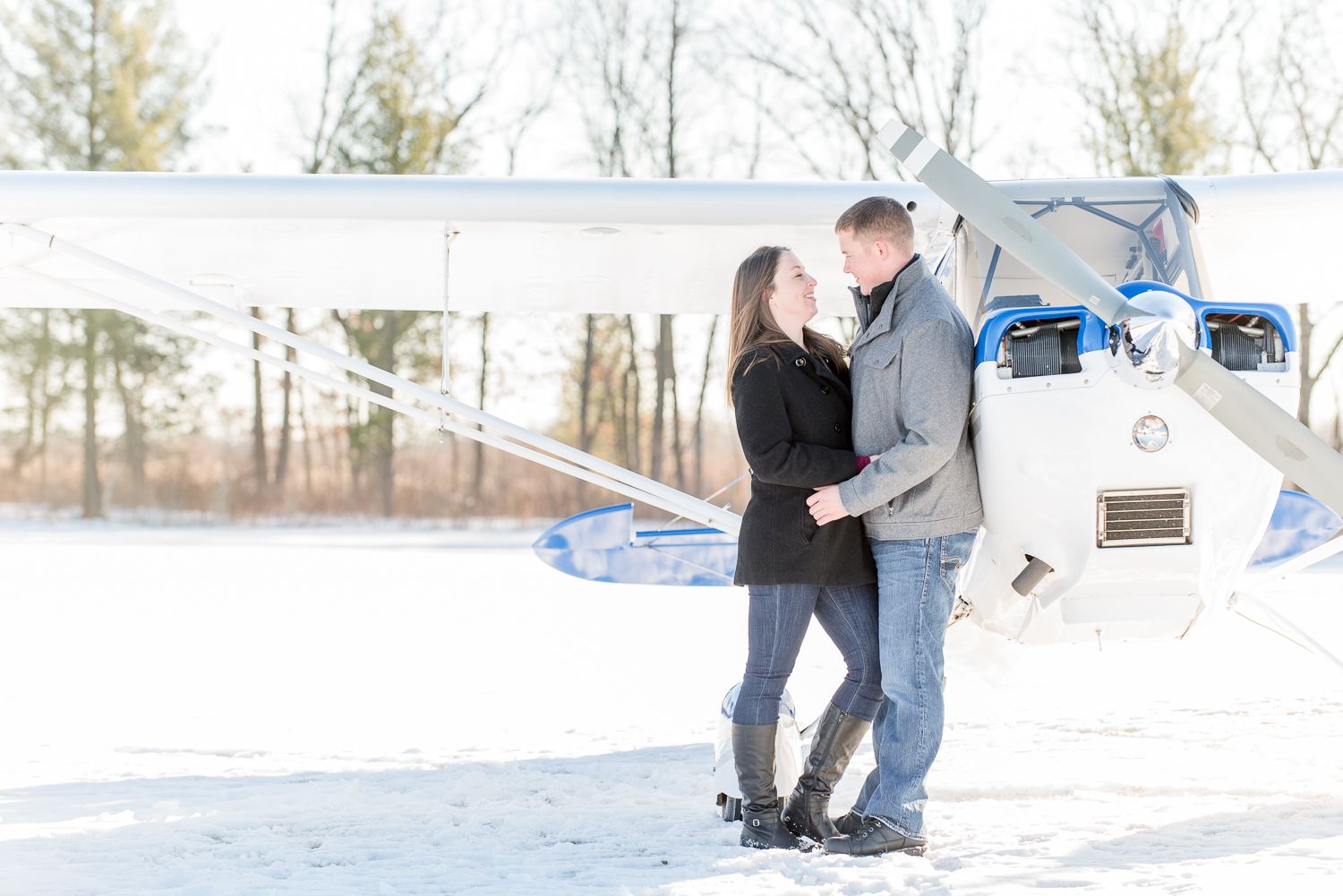 A couple embraces near a small aircraft on a snowy winter day.