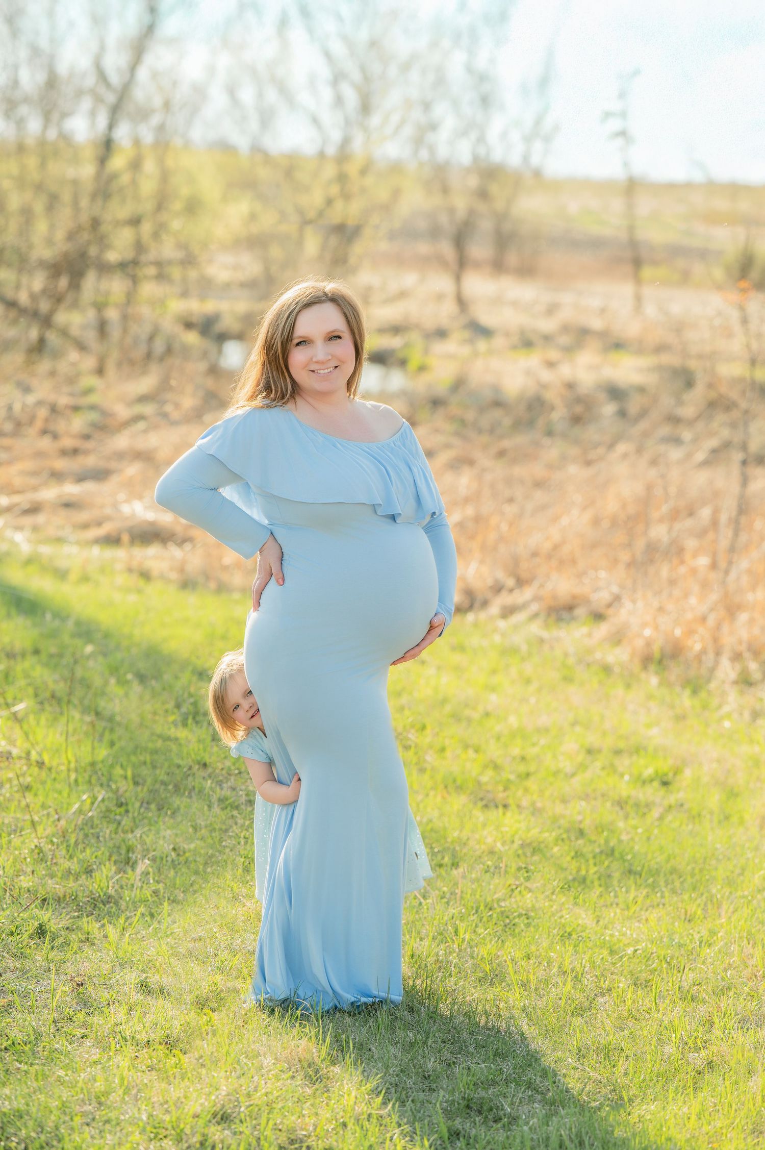 Maternity portrait in pale blue dress against natural spring landscape.