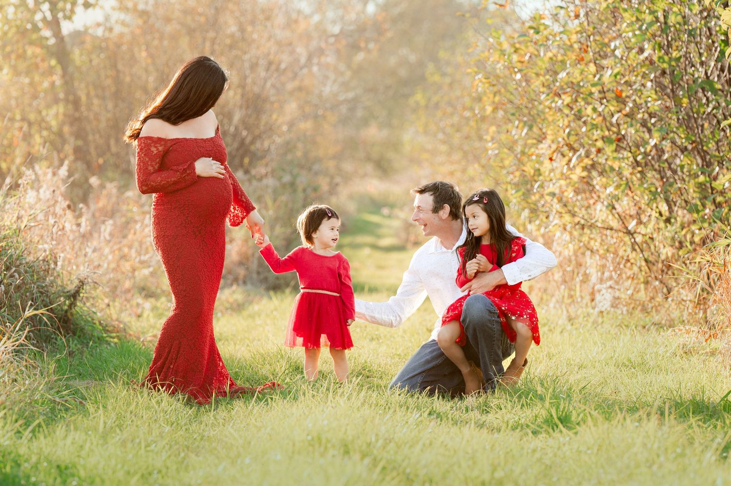 Family of four enjoying playful moment in autumn field with red outfits.