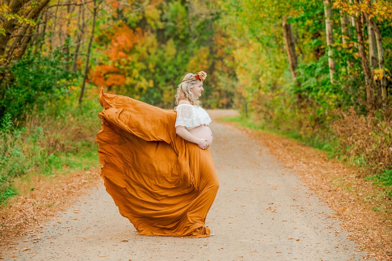 A flowing rust-colored dress billows dramatically on a fall forest path.