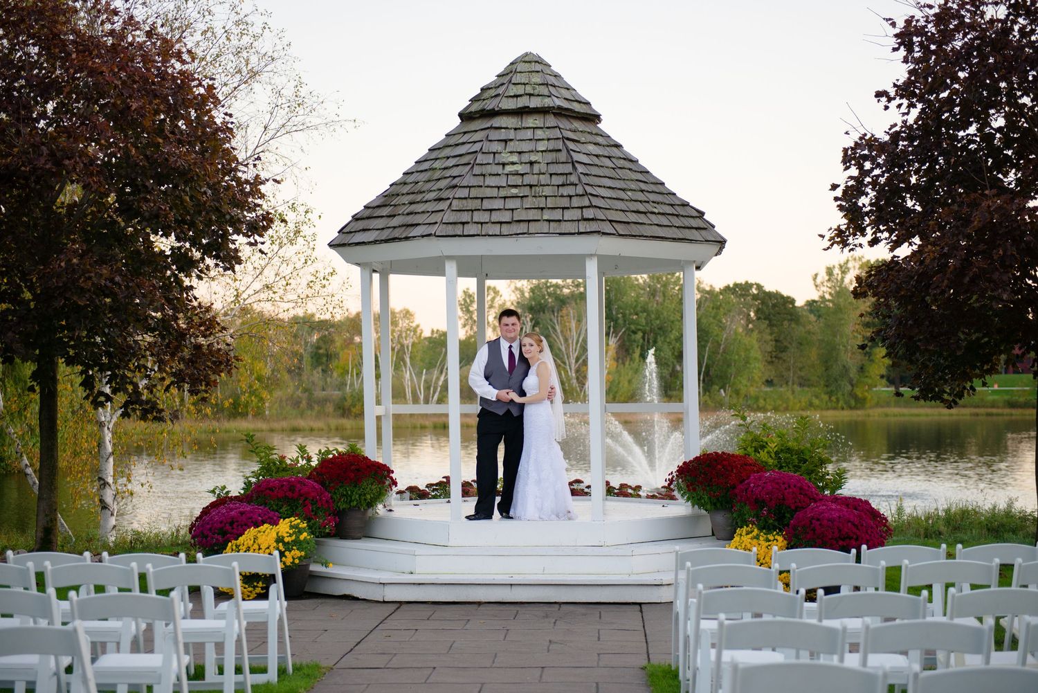 Outdoor wedding ceremony setup with white gazebo and seating arranged on a grassy lawn decorated with fall flowers. Andover wedding at Mages