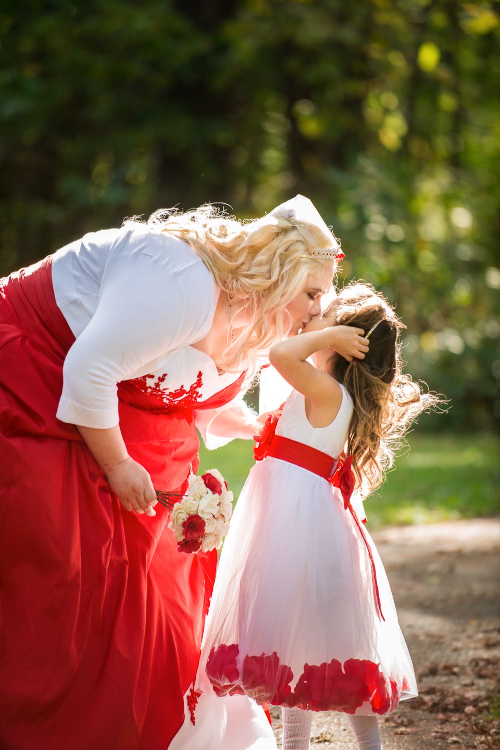 Dance partners in matching red and white dresses twirl together on a sunlit forest path.