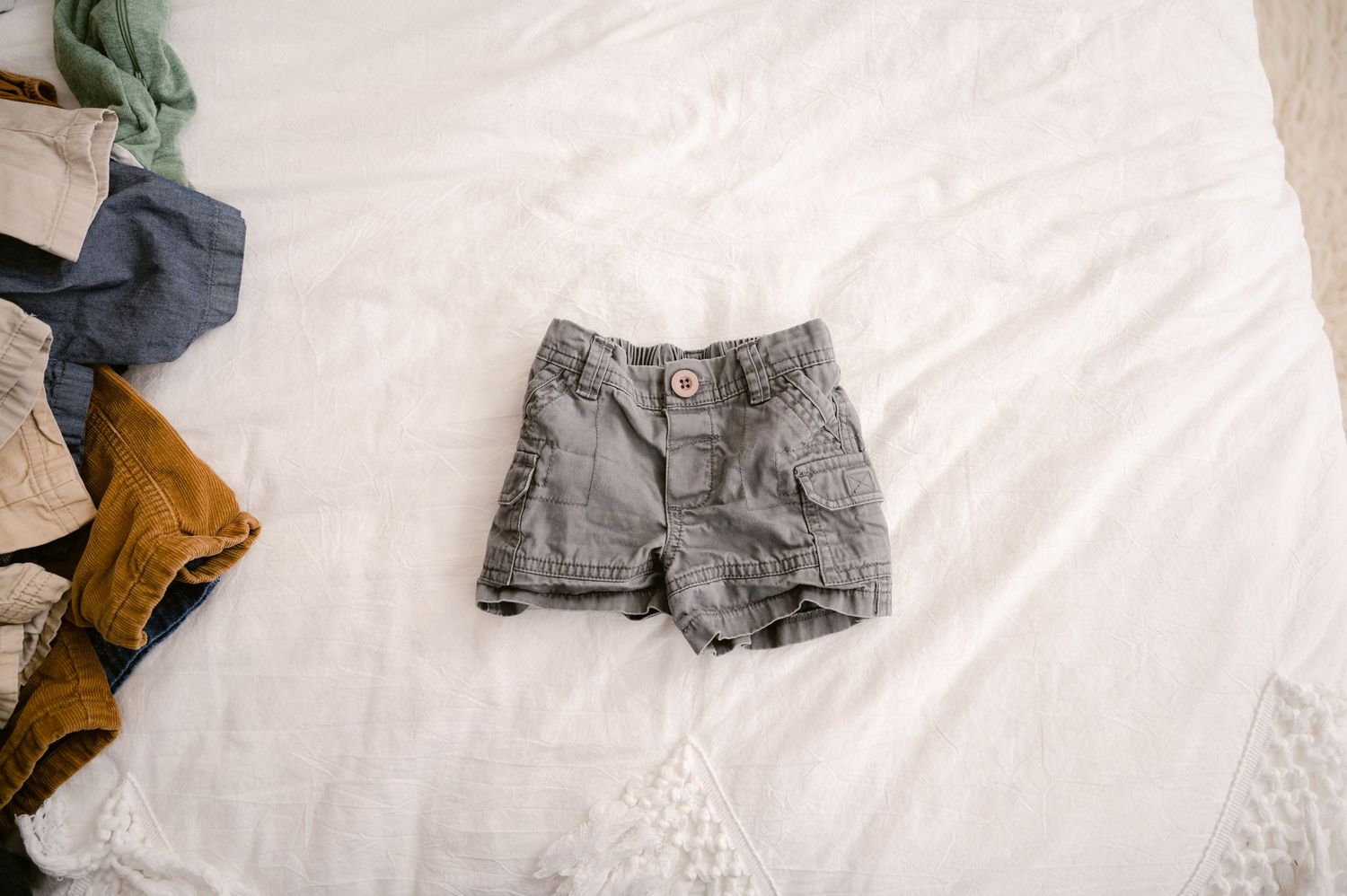 A pair of gray denim shorts lying flat on a white textured surface with other clothing items visible in the background.