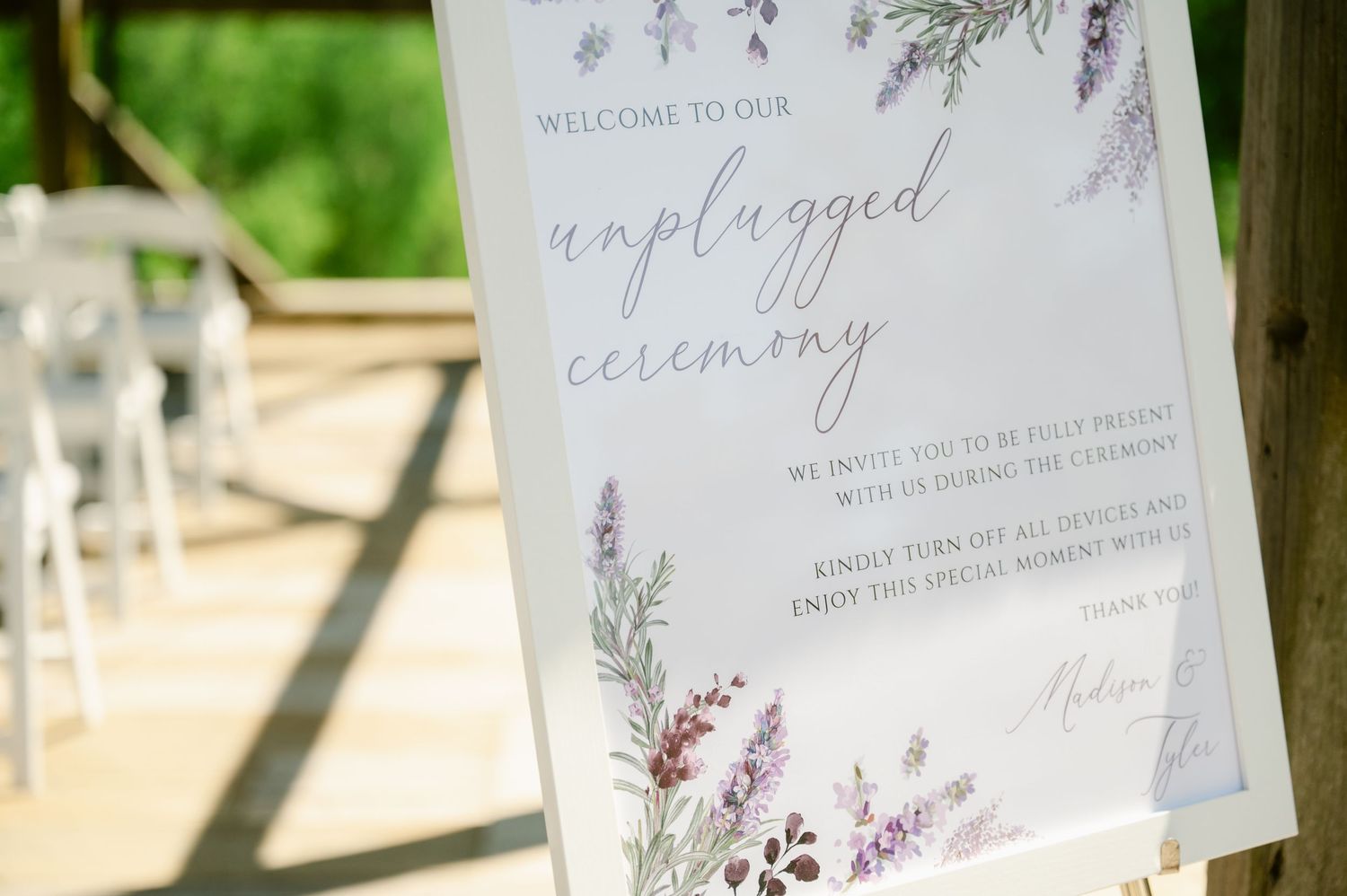 Close-up of an elegantly styled wedding ceremony sign with delicate watercolor floral details in purple and green tones.