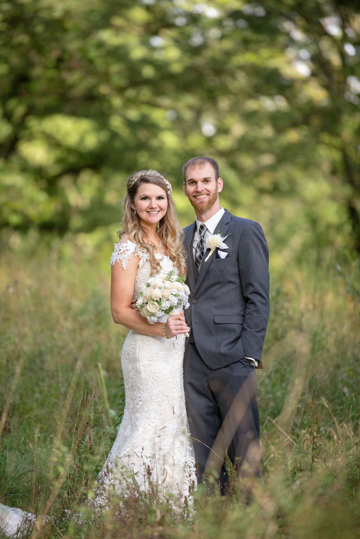 A wedding couple poses in a rustic field with natural greenery in the background. Rum River Barn Milaca Minnesota Weddings