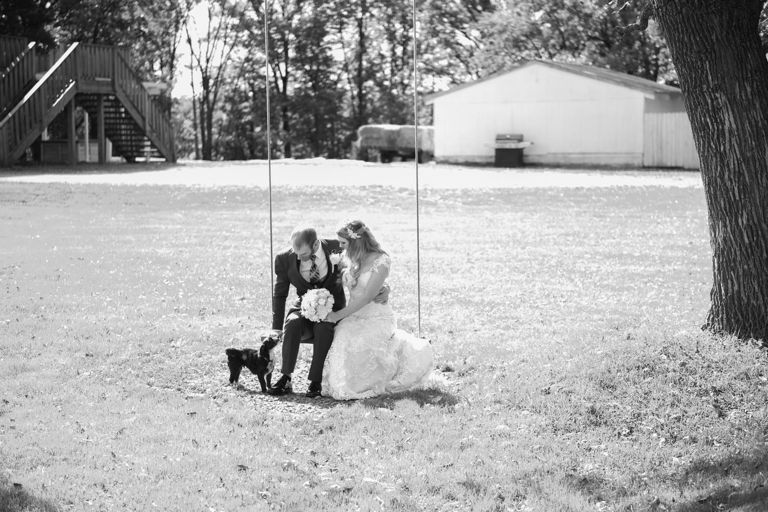 A black and white landscape photo shows people and pets relaxing under trees in the distance. Rum River Barn Milaca Minnesota Weddings