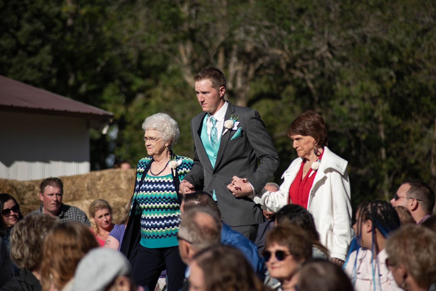 Outdoor wedding ceremony guests seated in rows on a sunny day with trees in the background.