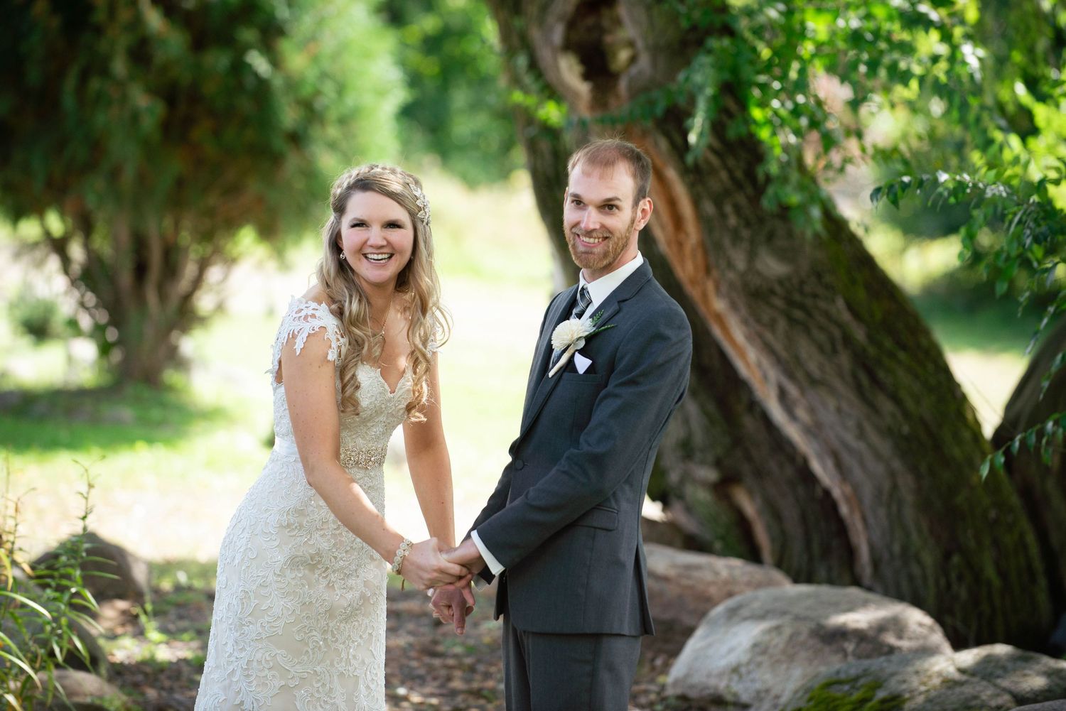 A newlywed couple poses for a romantic outdoor wedding photo under a large tree. Rum River Barn Milaca Minnesota Weddings