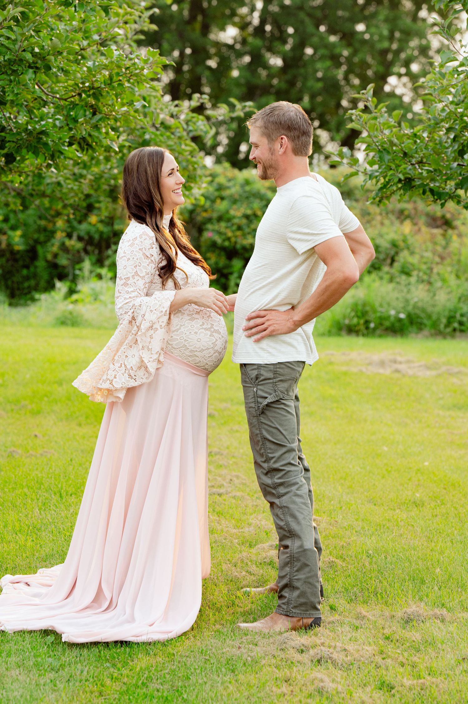 Couple sharing intimate moment during maternity photoshoot in garden setting.