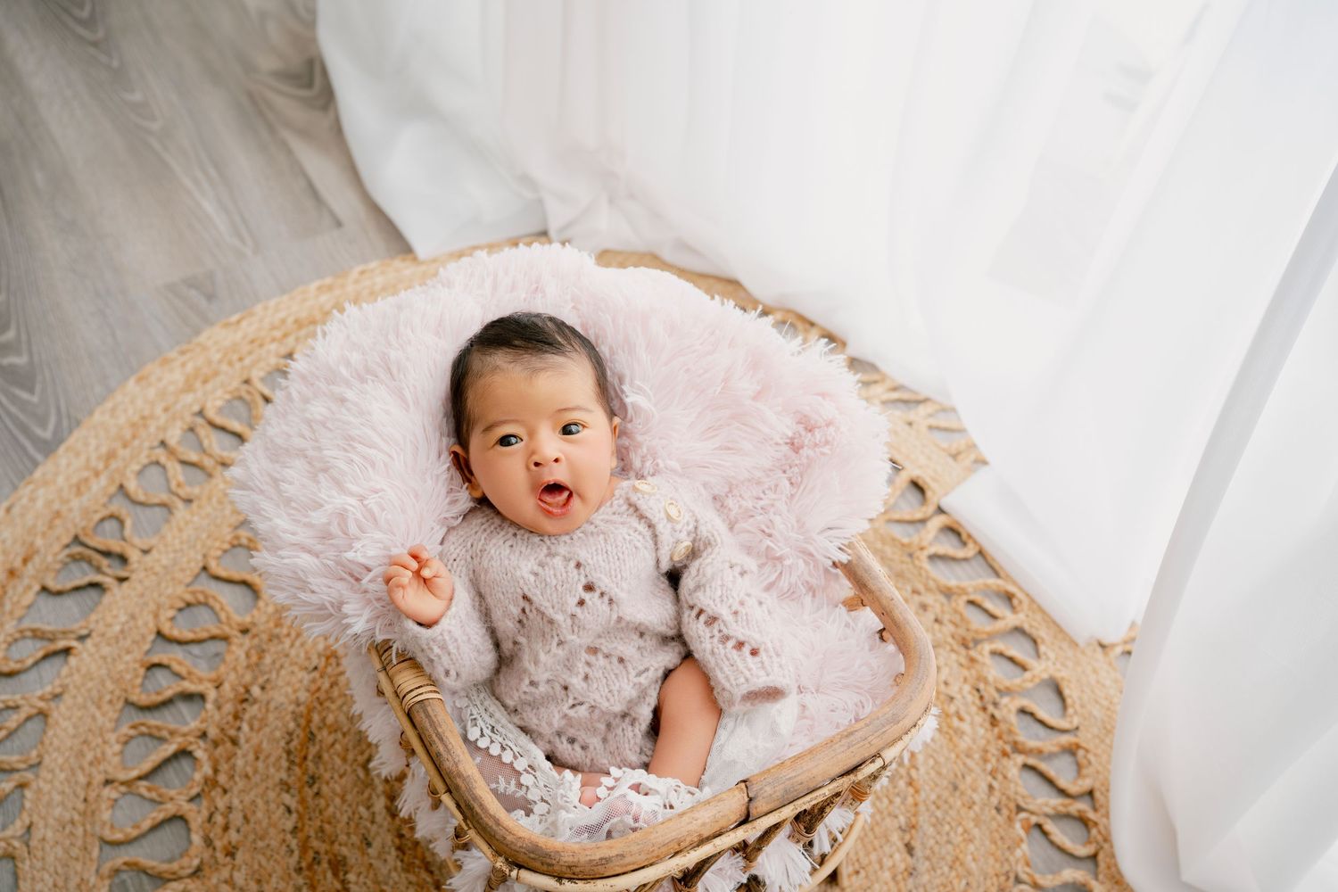 Baby lying on pink blanket in woven basket smiles during newborn photography session.