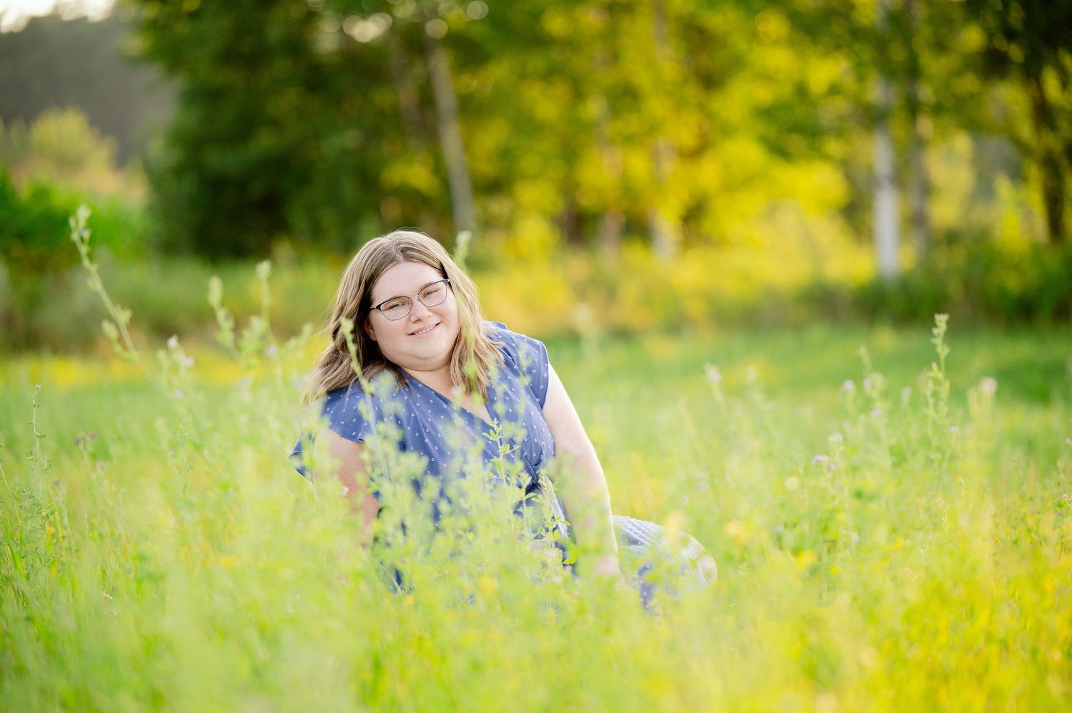 Senior Portrait in Foreston MN lying in a summer wildflower meadow surrounded by tall yellow flowers and green grass in warm sunlight.
