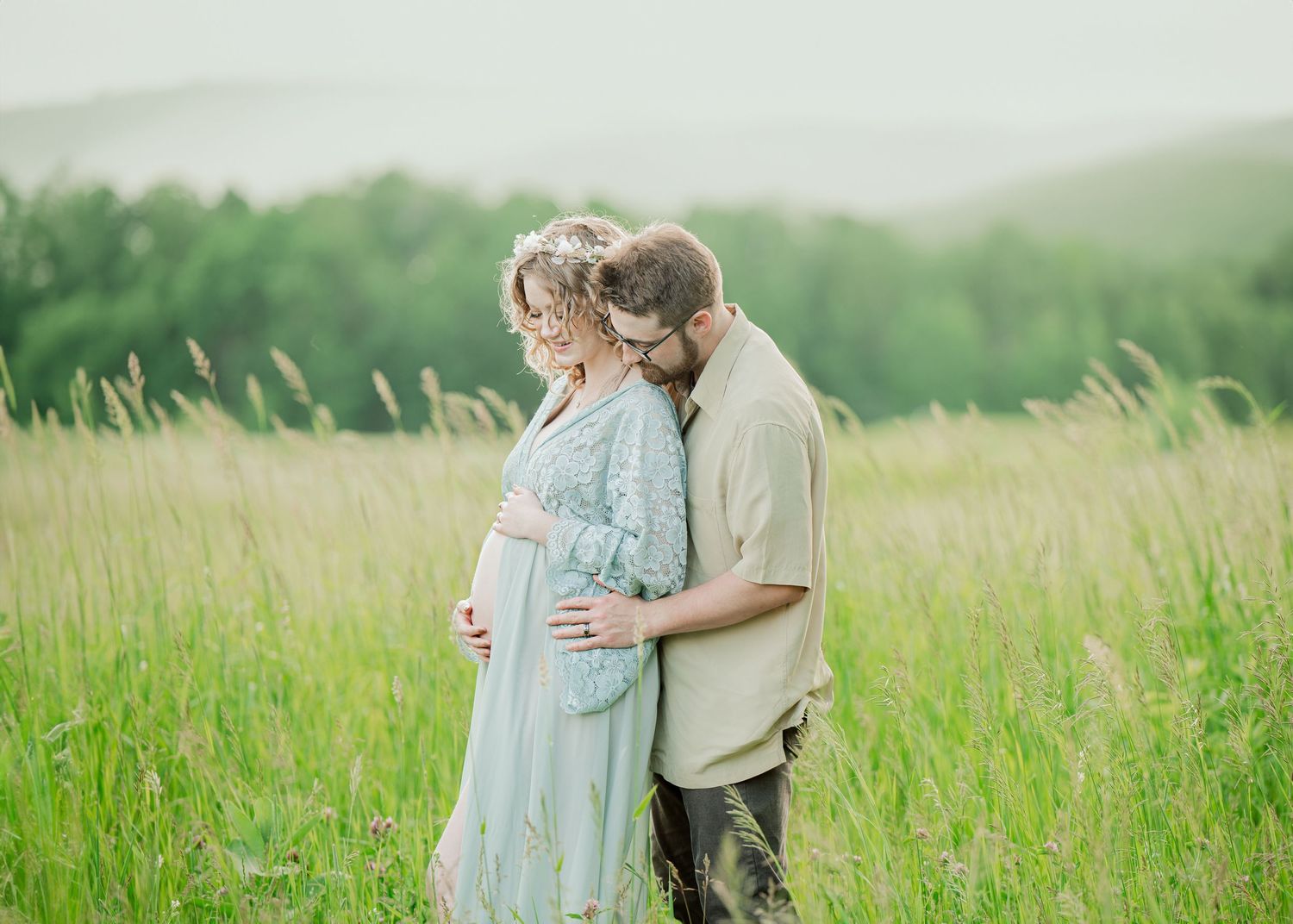 Intimate maternity moment captured in sun-lit meadow with mountains in background.