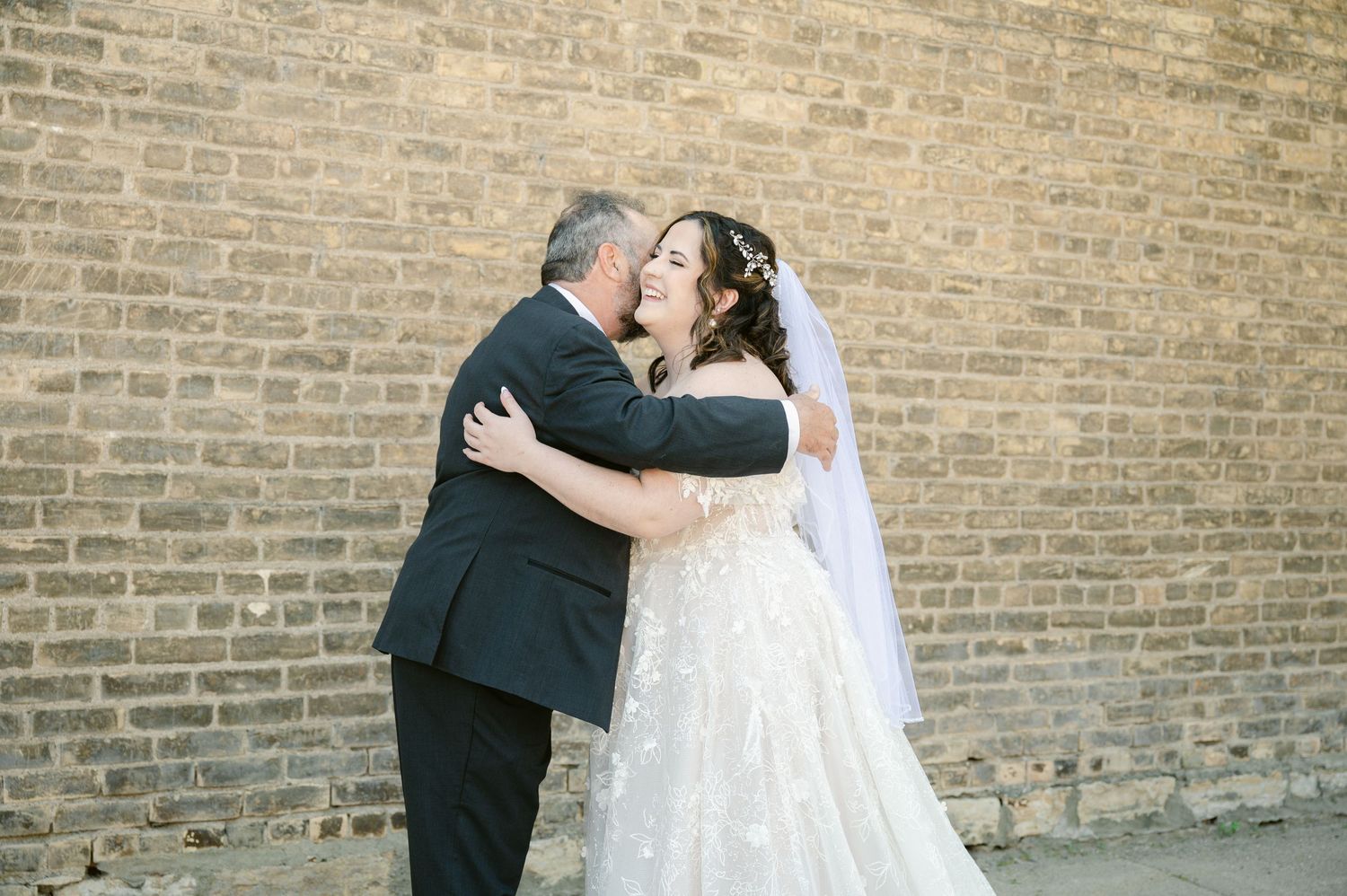 A tender embrace between newlyweds against a brick wall background.