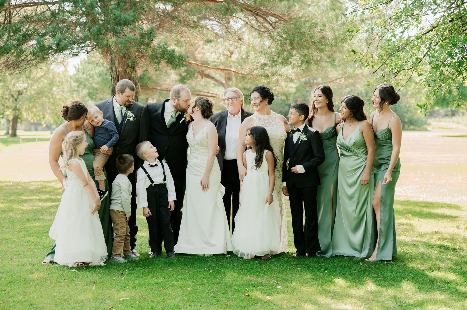 The Grands at Mulligans- Wedding Photos: Wedding party poses for group photos on a grassy lawn under green trees.