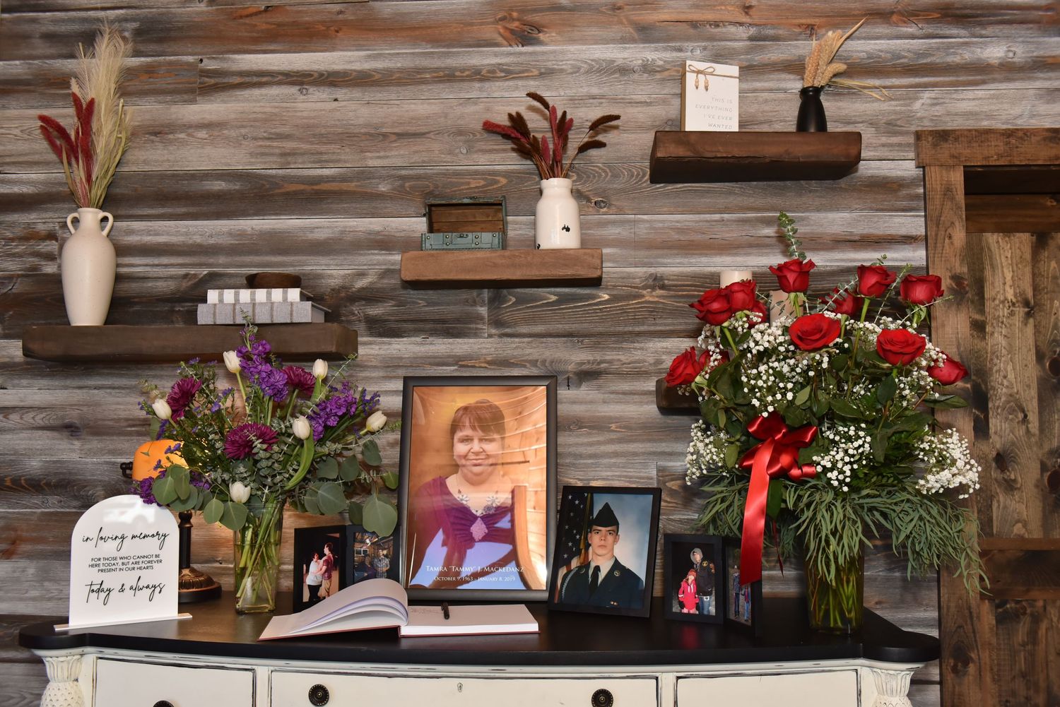 Rustic wooden wall decorated with floral arrangements and photo frames displaying family memories.