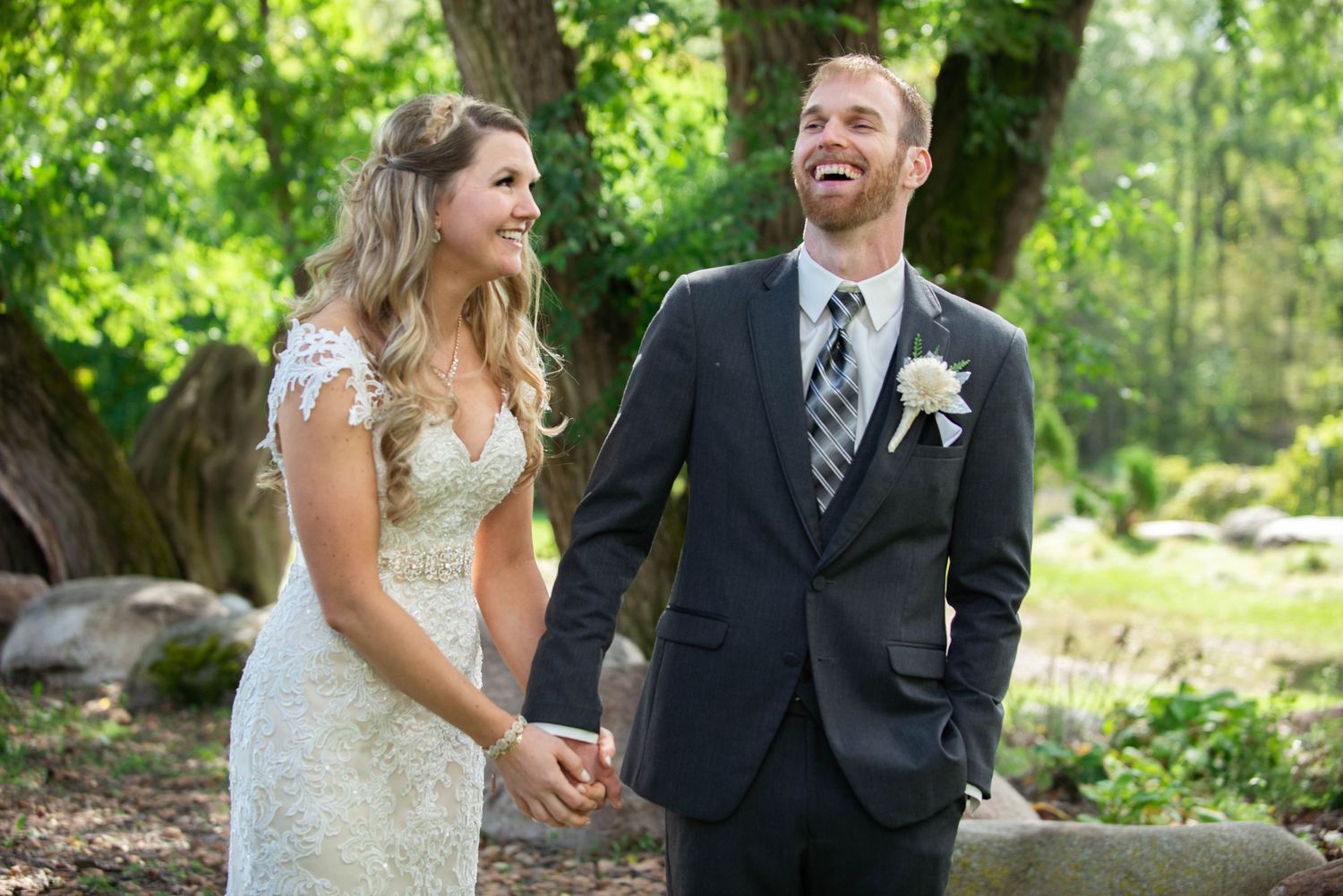 Happy couple sharing joyful laughs during outdoor wedding photo session in lush garden setting. Rum River Barn Milaca Minnesota Weddings