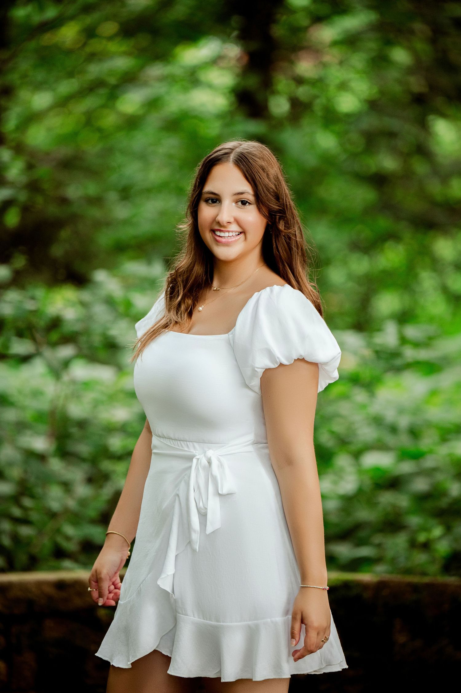 Senior Portrait in Central MN in white cotton dress with cap sleeves poses against verdant garden background.
