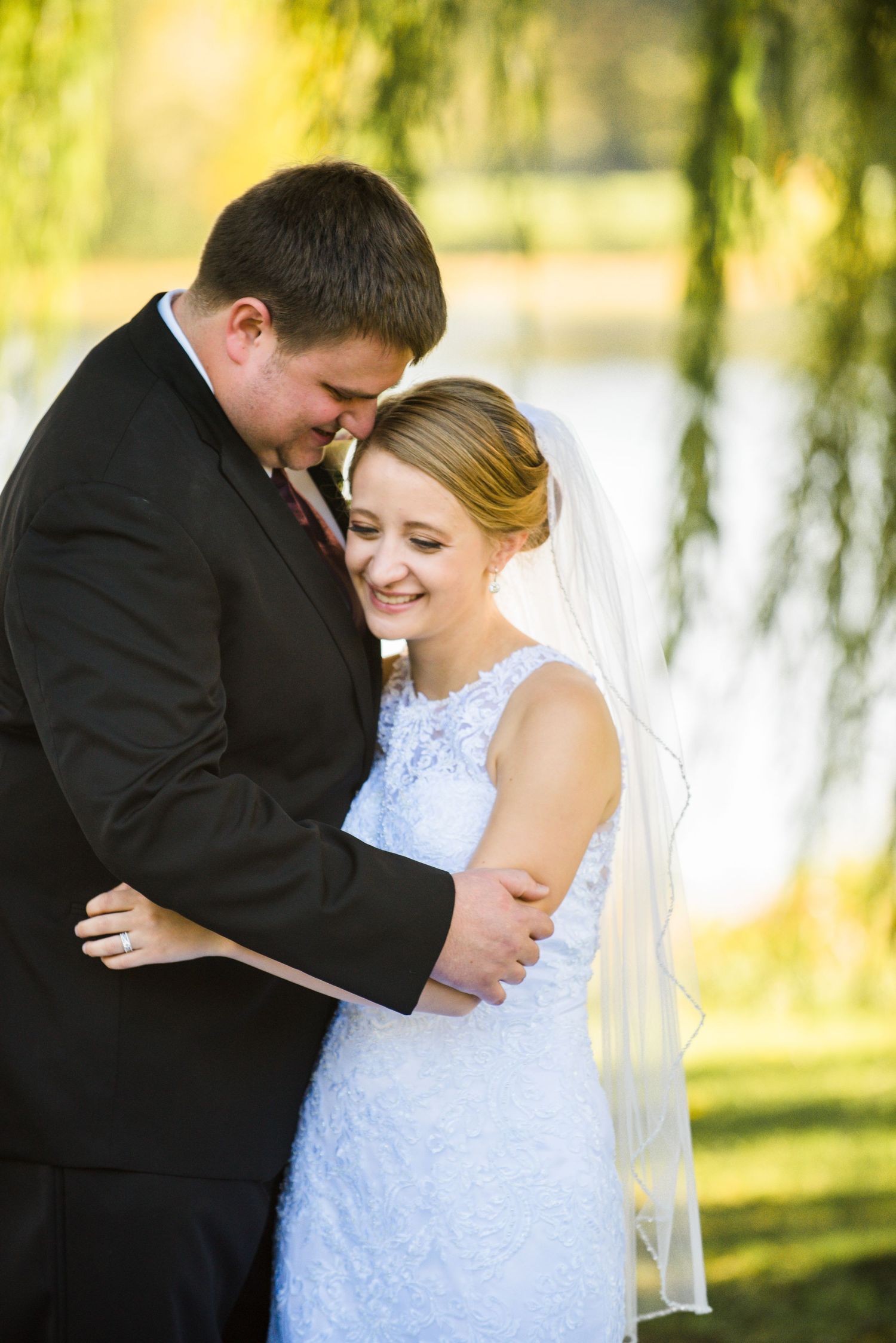Tender moment between newlyweds sharing a laugh under drooping willow branches. Andover wedding at Magestic Oaks Golf Club