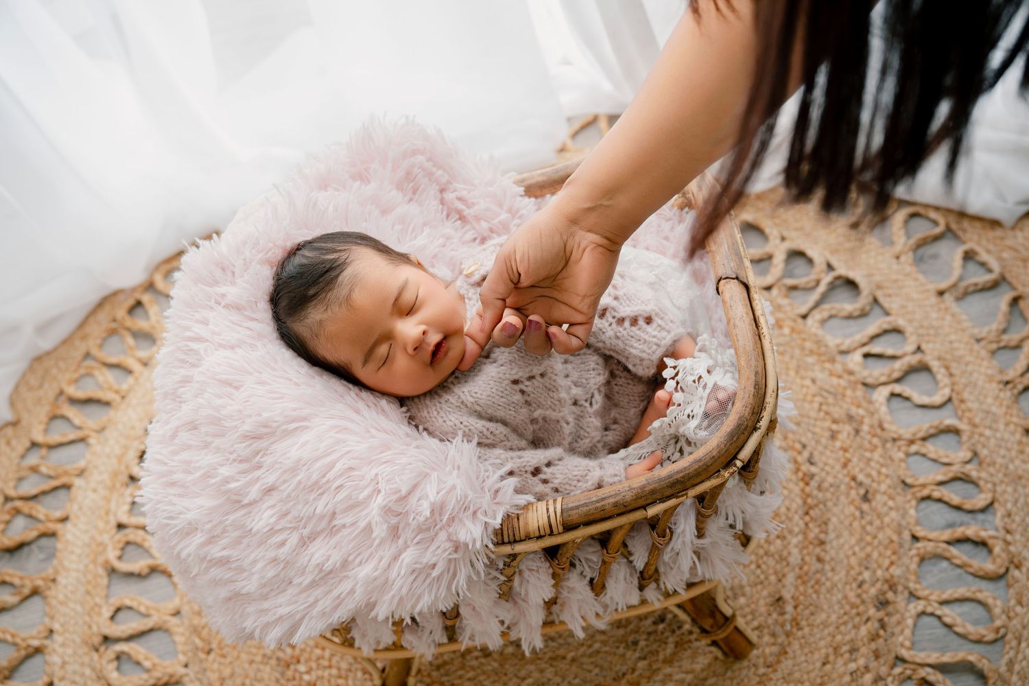 Sleeping newborn baby rests peacefully on pink fluffy blanket in wicker basket during professional photo session.