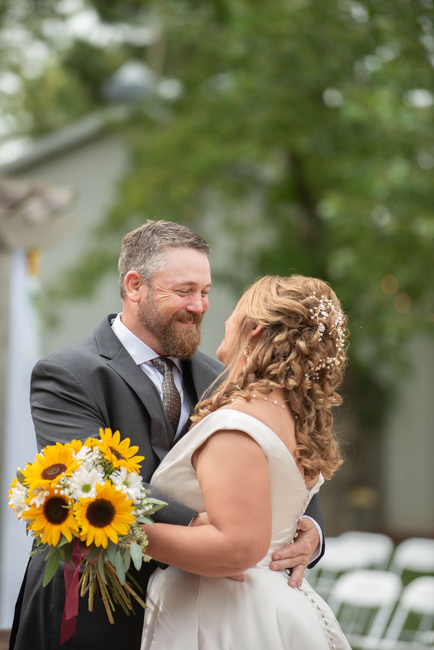 A joyous outdoor wedding moment with sunflowers in the bride's bouquet as the happy couple embraces.