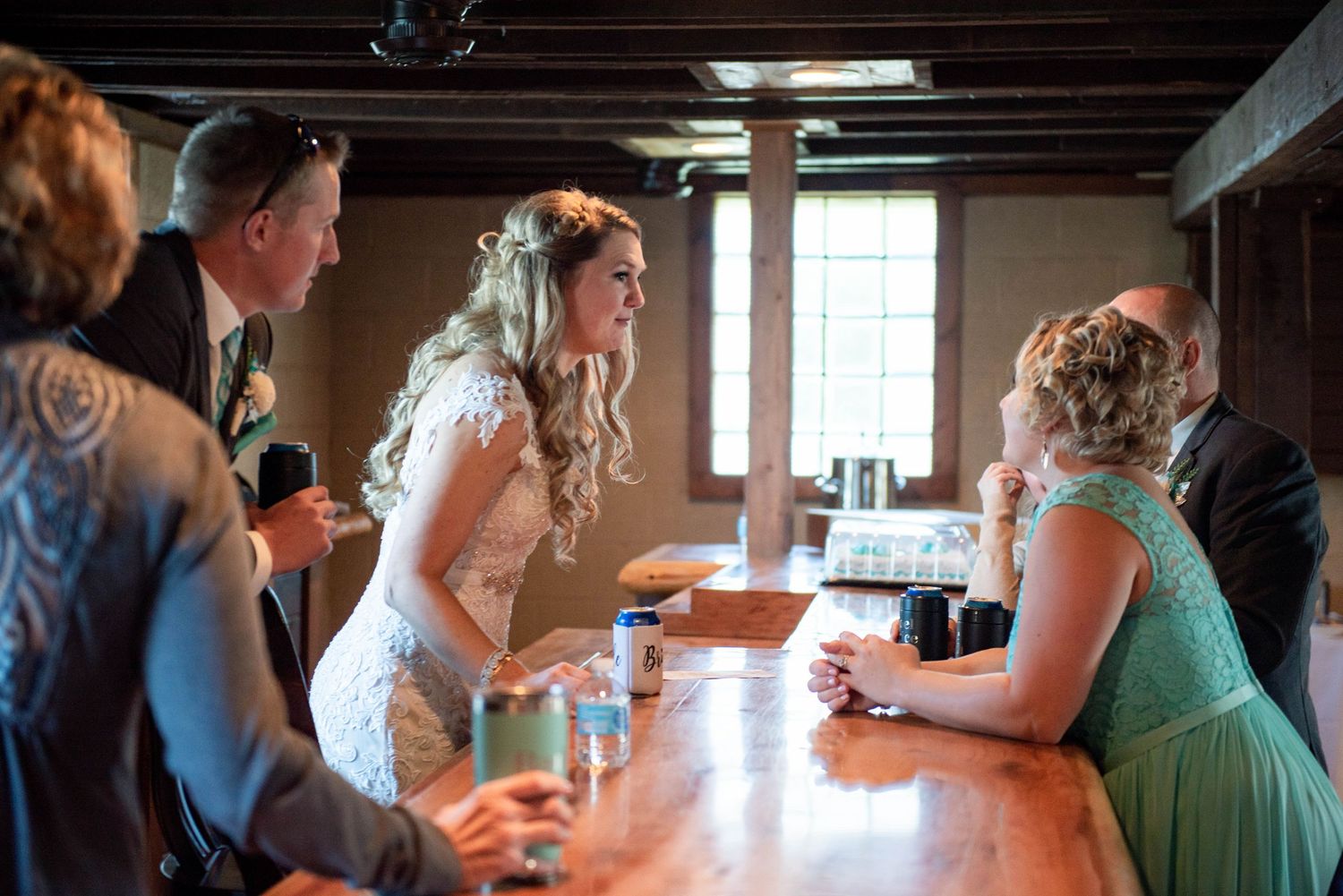 Wedding reception gathering at rustic wooden bar with bride and guests. Rum River Barn Milaca Minnesota Weddings