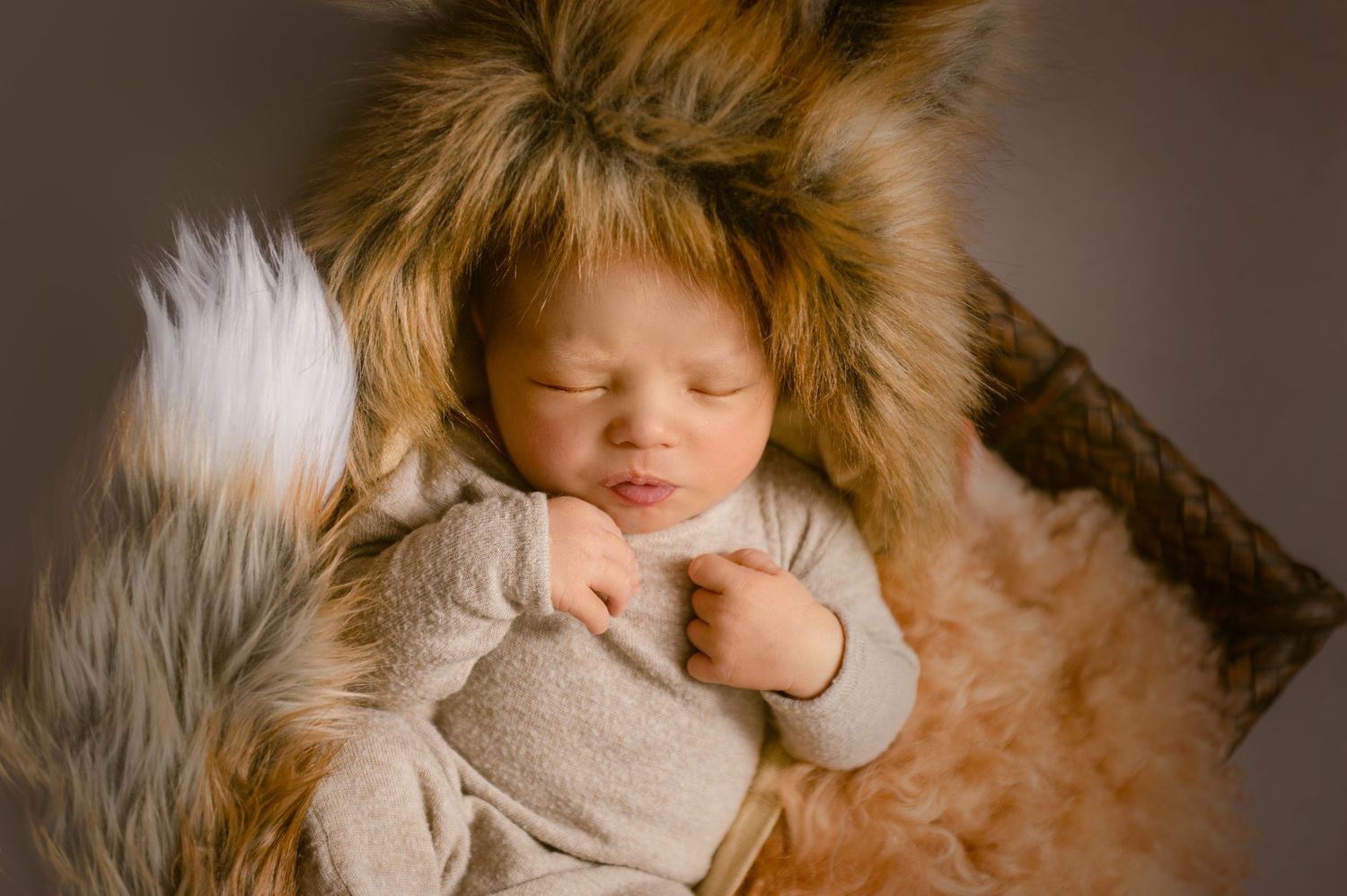 Peaceful sleeping infant wearing cozy fur-lined hood and beige outfit.