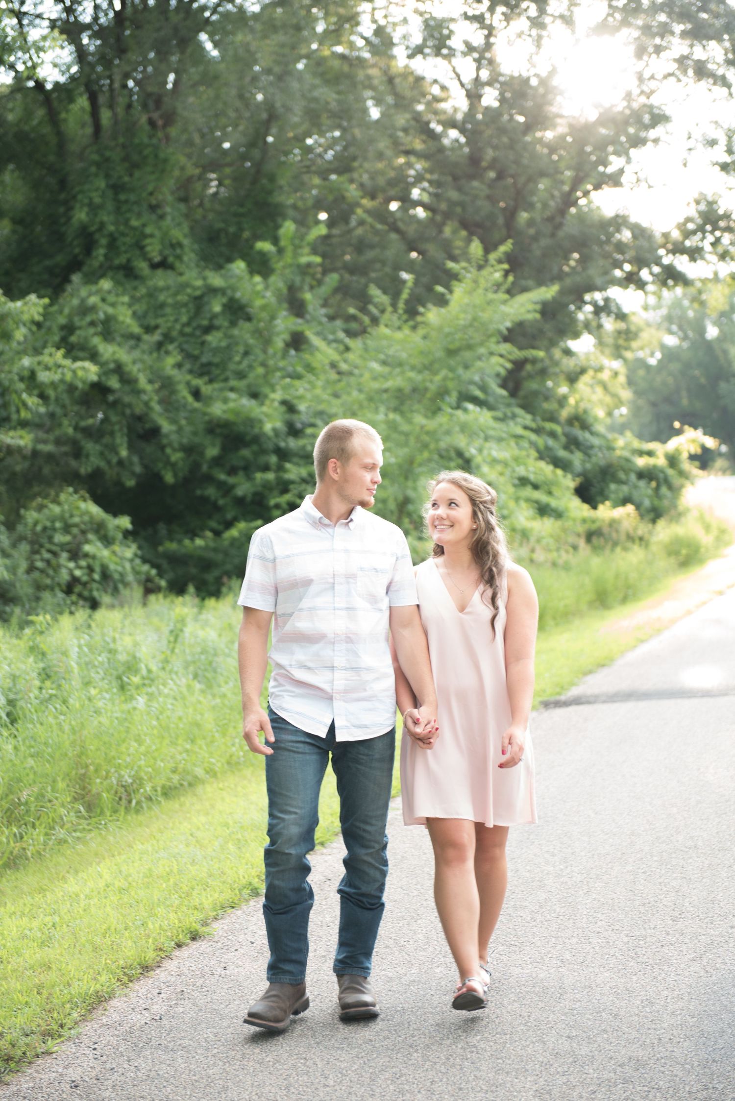 A couple walks together on a sunlit path surrounded by lush greenery on a summer evening.