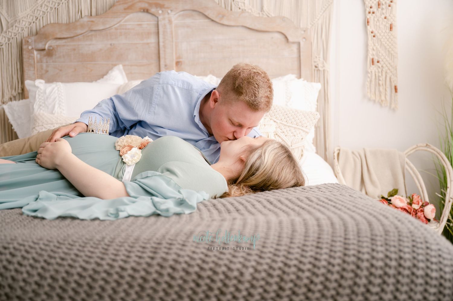 A couple lies together intimately on a bed with gray bedding and decorative headboard in a romantic setting.